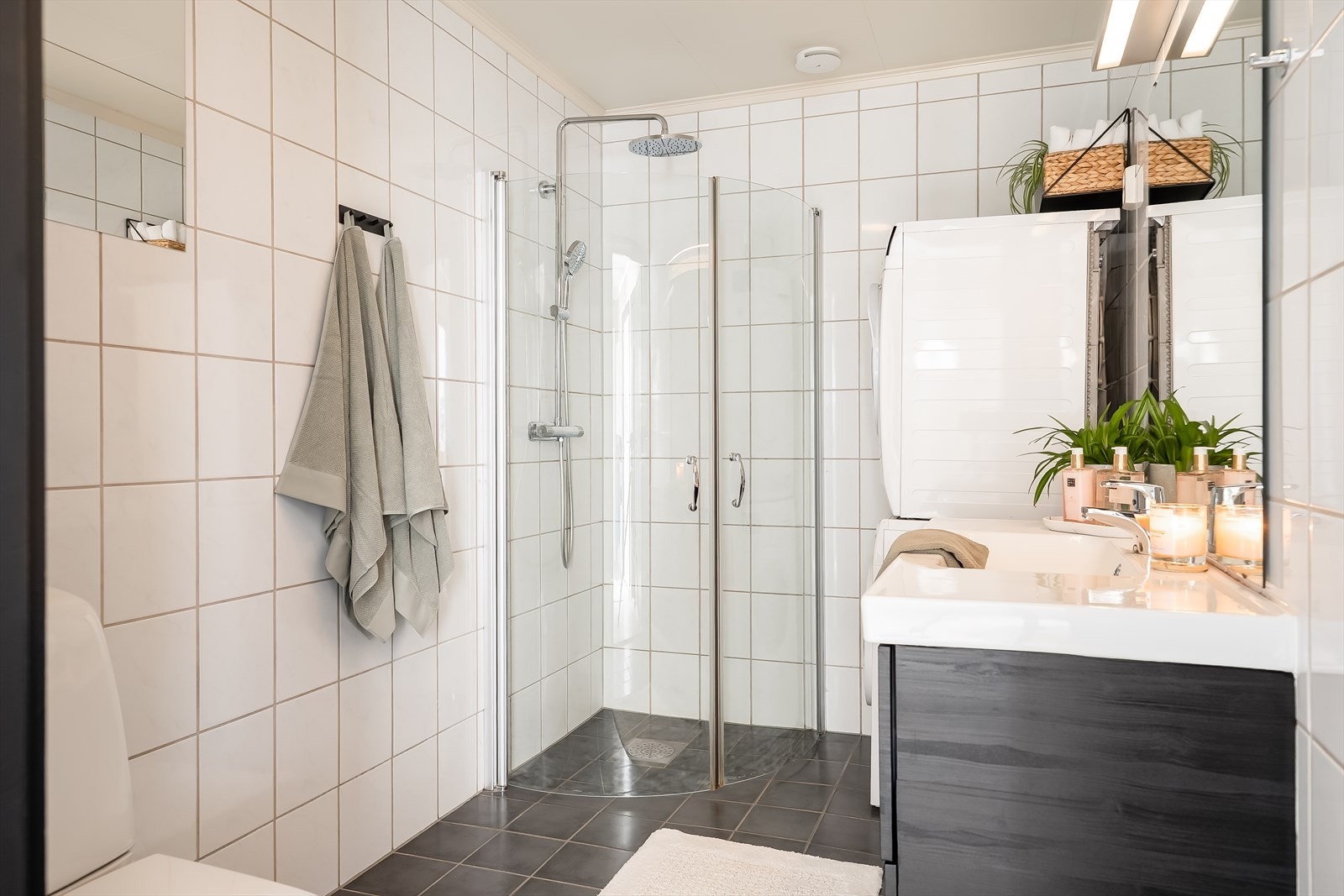 Lyst baderom utstyrt med dusjhjørne med innfellbare dusjdører, servantinnredning og toalett. Galleribilde