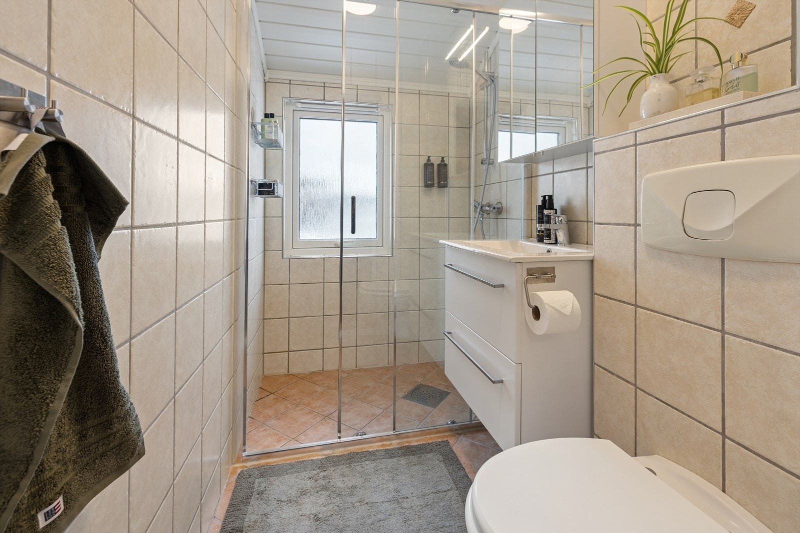 Baderom med veggmontert toalett, servant med innredning og dusjnisje. Galleribilde