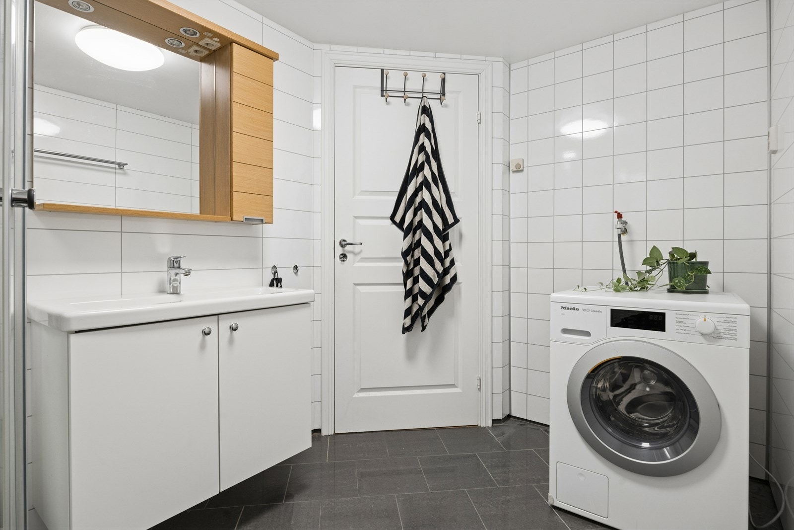 Badet er utstyrt med dusjkabinett, gulvmontert toalett, stilren innredning med servant, samt opplegg for vaskemaskin med både kran og avløp. Galleribilde