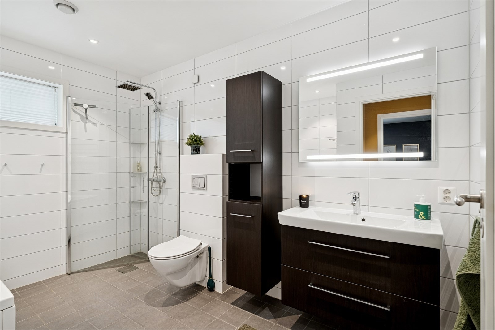 Badet i 1. etasje er flislagt og utstyrt med varmekabler i gulv, vegghengt toalett, servant med innredning, badekar og dusjløsning. Galleribilde