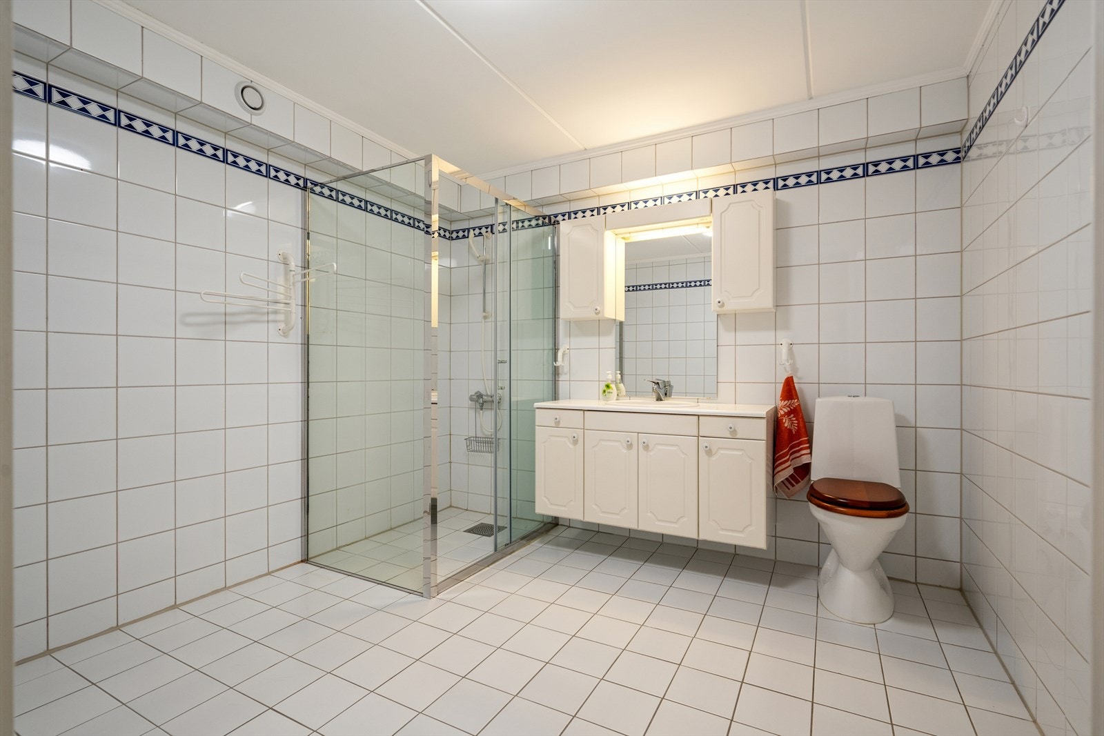 Baderom innredet med toalett, baderomsinnredning med servant og en dusjløsning med dusjvegger. Galleribilde