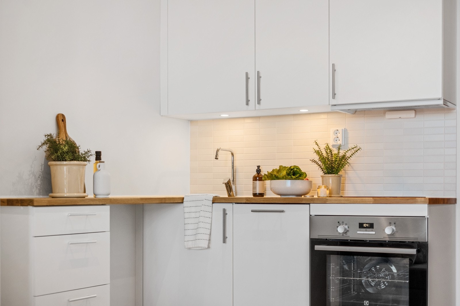 Kjøkkenet er stilrent med hvite slette fronter, laminat benkeplate med nedfelt vask og fliser på vegg over benk Galleribilde