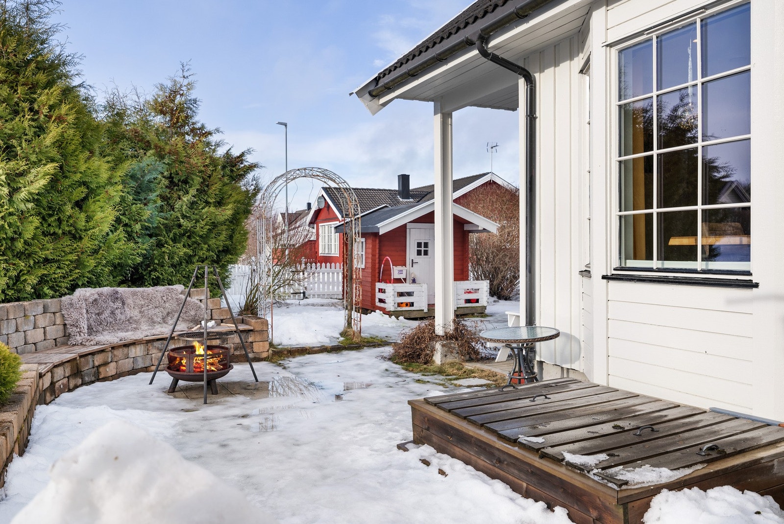 Uteområde med bålplass og sittebenk. Rød lekestue i bakgrunnen. Galleribilde