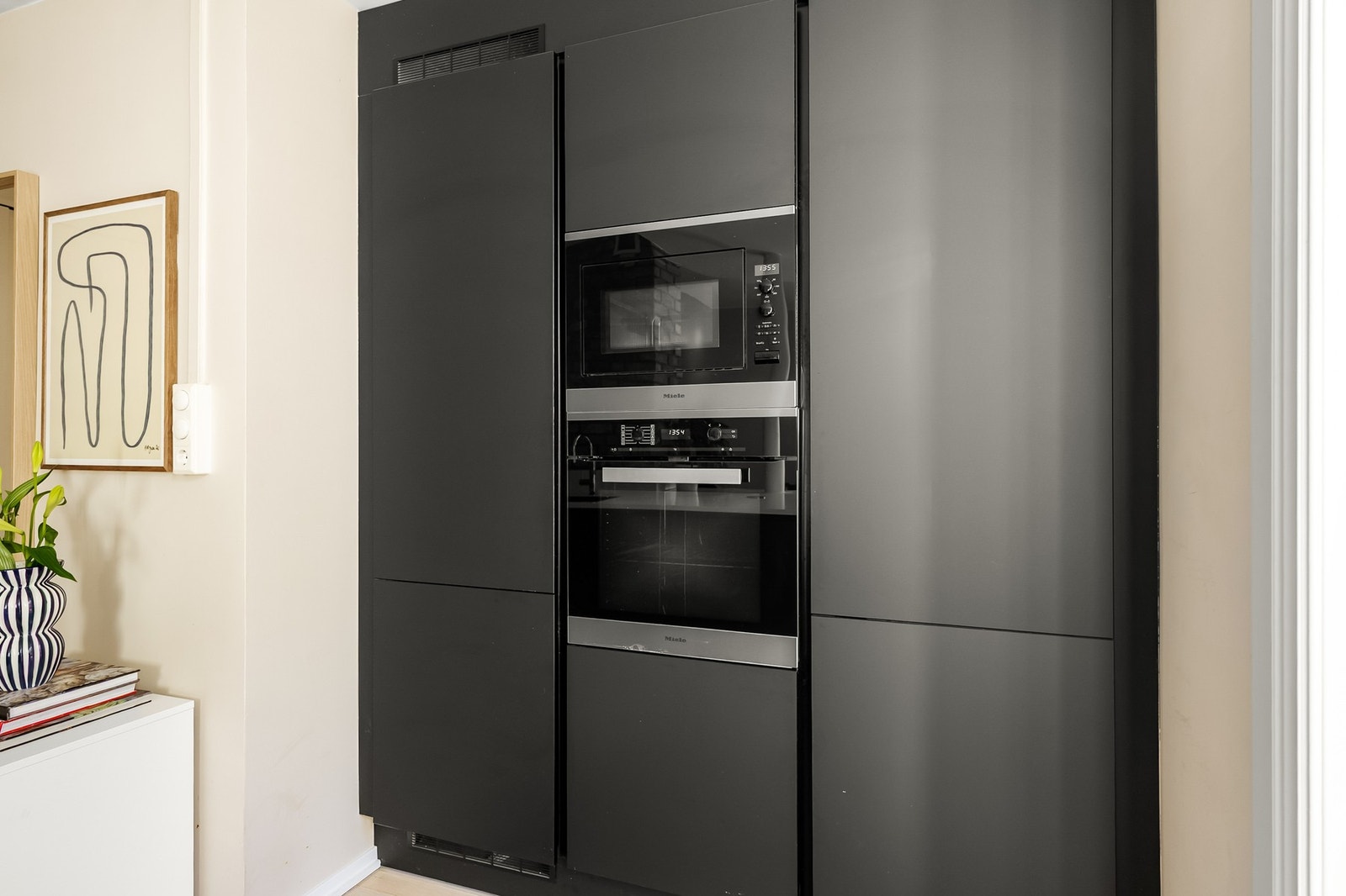 Integrerte hvitevarer fra Miele som oppvaskmaskin, kjøl/frys, stekeovn og micro i høyskap, og induksjonsplatetopp med integrert avtrekksvifte (kullfilter). Galleribilde