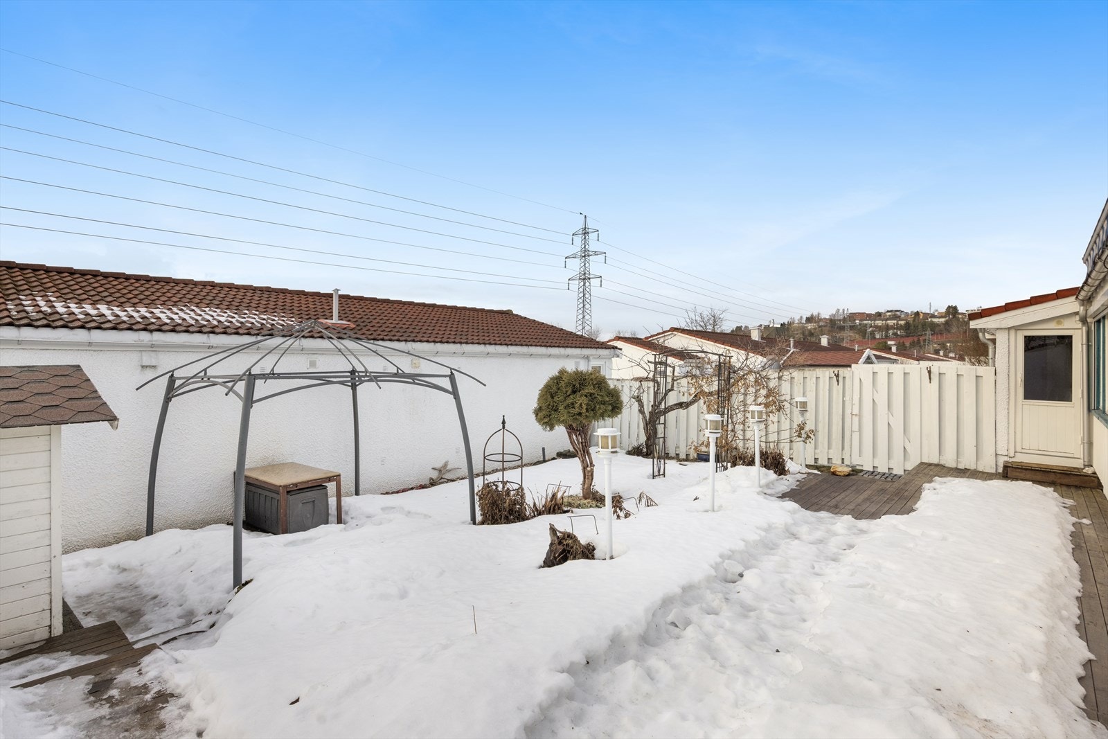 Inngjerdet og solrikt uteområde pent oppbareidet med med blant annet terrasser, paviljong, lykter, blomsterbed og hagebod. Galleribilde