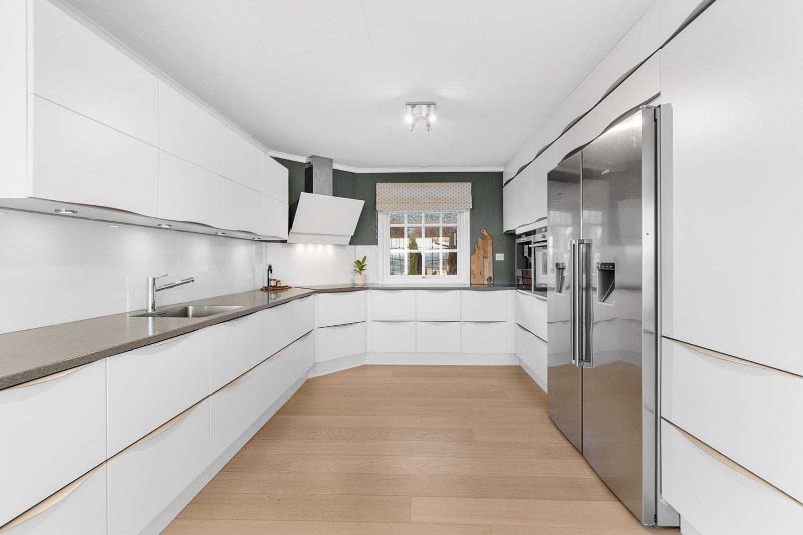 Romslig kjøkken med slette, hvite fronter og laminat benkeplate med nedfelt vask i stål. Galleribilde