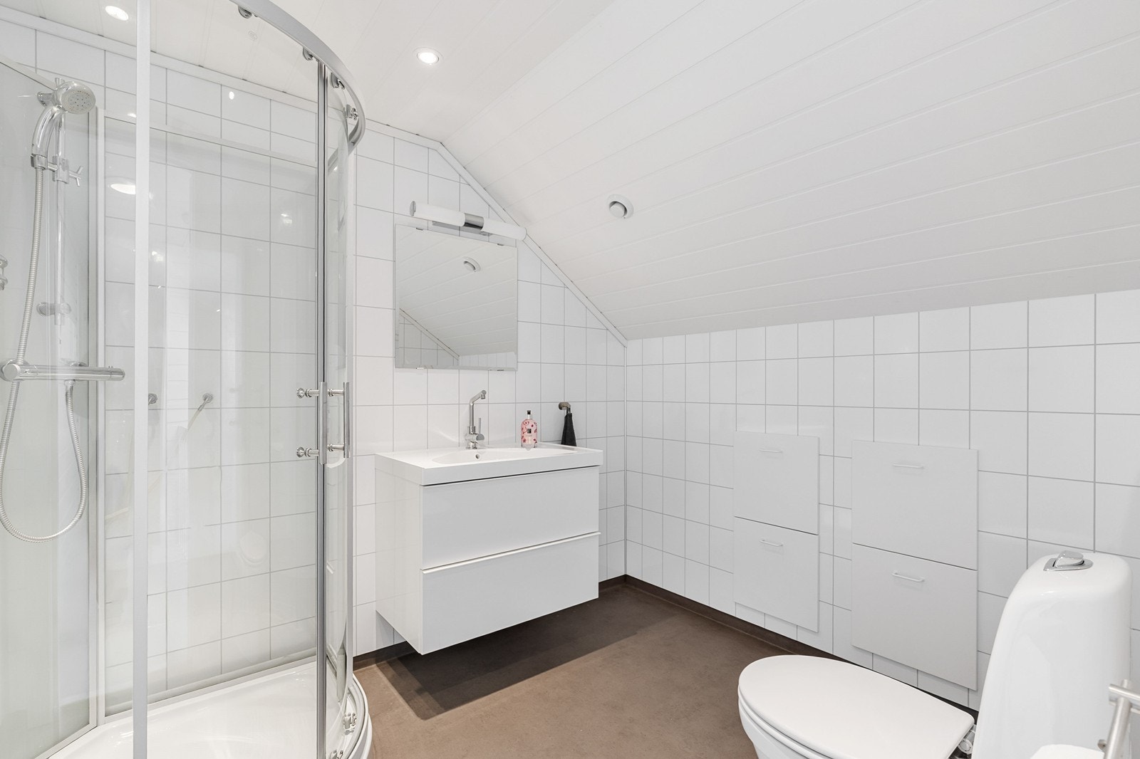 Lyst og pent bad innredet med gulvstående toalett, servant med skuffeinnredning og dusjkabinett. Galleribilde