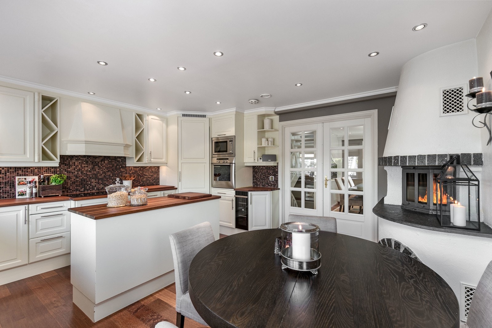 Kjøkkeninnredning med lyse profilerte fronter. Benkeplate av heltre i Merbau med underlimt kum. Av integrerte hvitevarer medfølger det bred induksjonsplatetopp med ovenhengt ventilator, oppvaskmaskin, vinskap, stekeovn og mikro. Stort kjølehjørne. Galleribilde