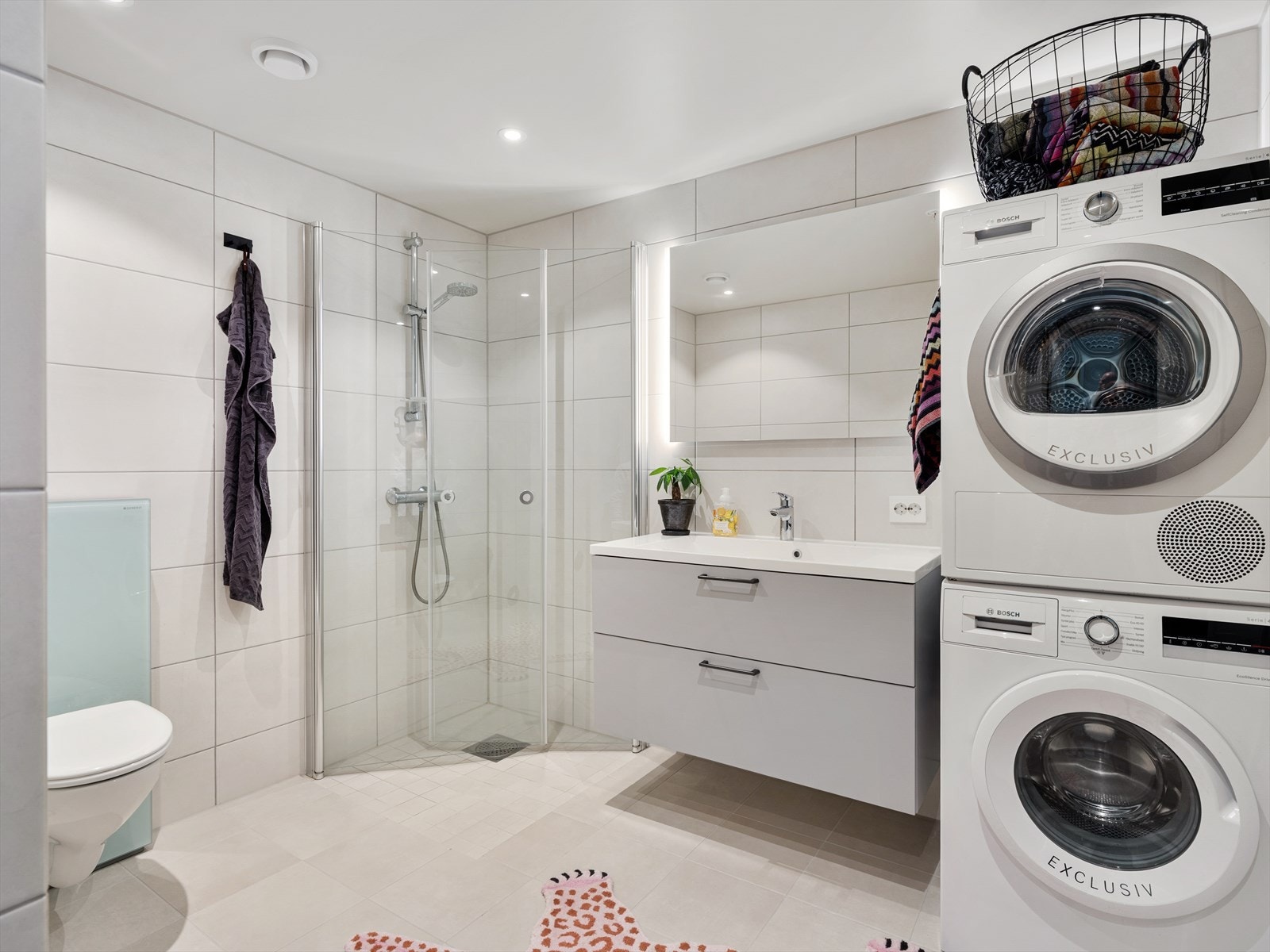 Flislagt baderom med toalett, dusjvegger som kan foldes mot vegg, servant i skuffeseksjon og opplegg til vaskemaskin. Galleribilde