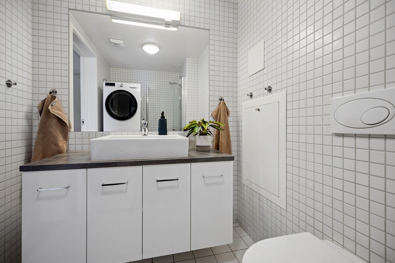 Rommet er innredet med servant på benkeplate med tilhørende servantskap, et veggfestet toalett med skjult sisterne og en dusj med innfellbare glassdører og nedsenket gulv i dusjsonen. Det er også opplegg for vaskemaskin. Galleribilde