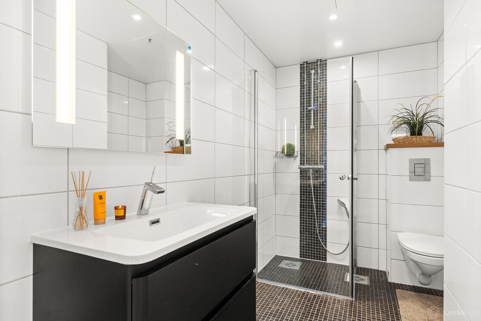 Baderommet | Lyst og pent bad innredet med servant med skuffer, speil m/belysning, veggmontert toalett og dusjhjørne. Galleribilde