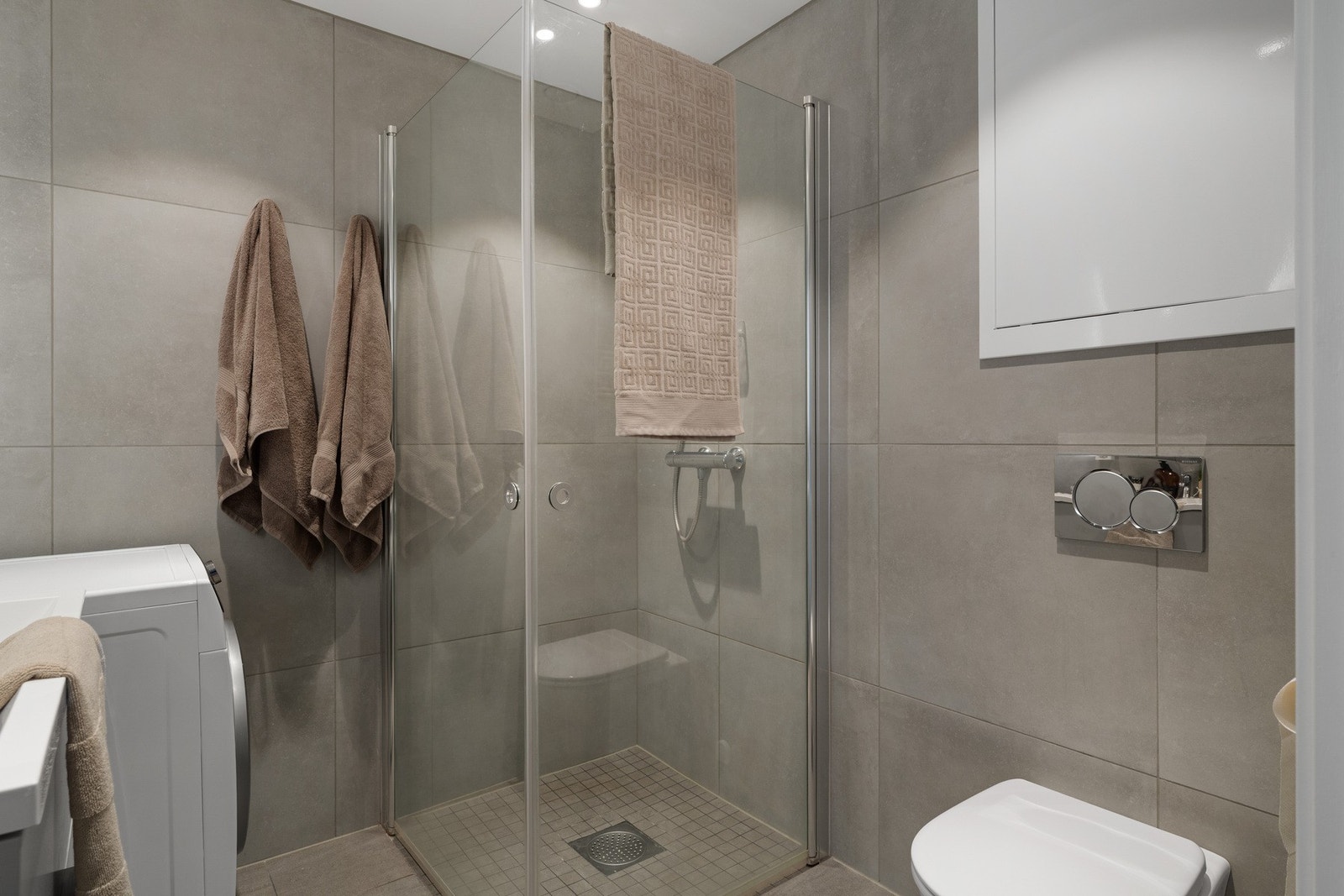 Badet har romslig dusjsone med glassvegger og stilrene flislagte overflater. Galleribilde