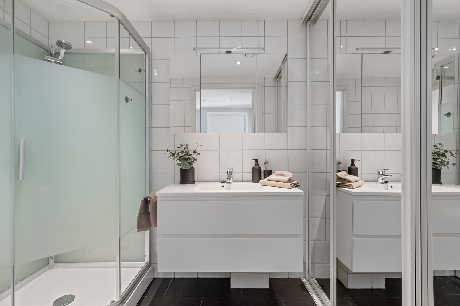 Flislagt baderom med dusjkabinett, vegghengt servant og spotter i tak. Galleribilde