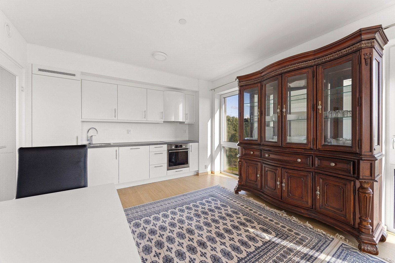 Moderne og stilrent kjøkken fra 2022 i åpen løsning mot stuen. Kjøkkeninnredningen består av hvite glatte fronter med belysning under overskap og laminat benkeplate med nedfelt oppvaskkum i rustfritt stål. Galleribilde