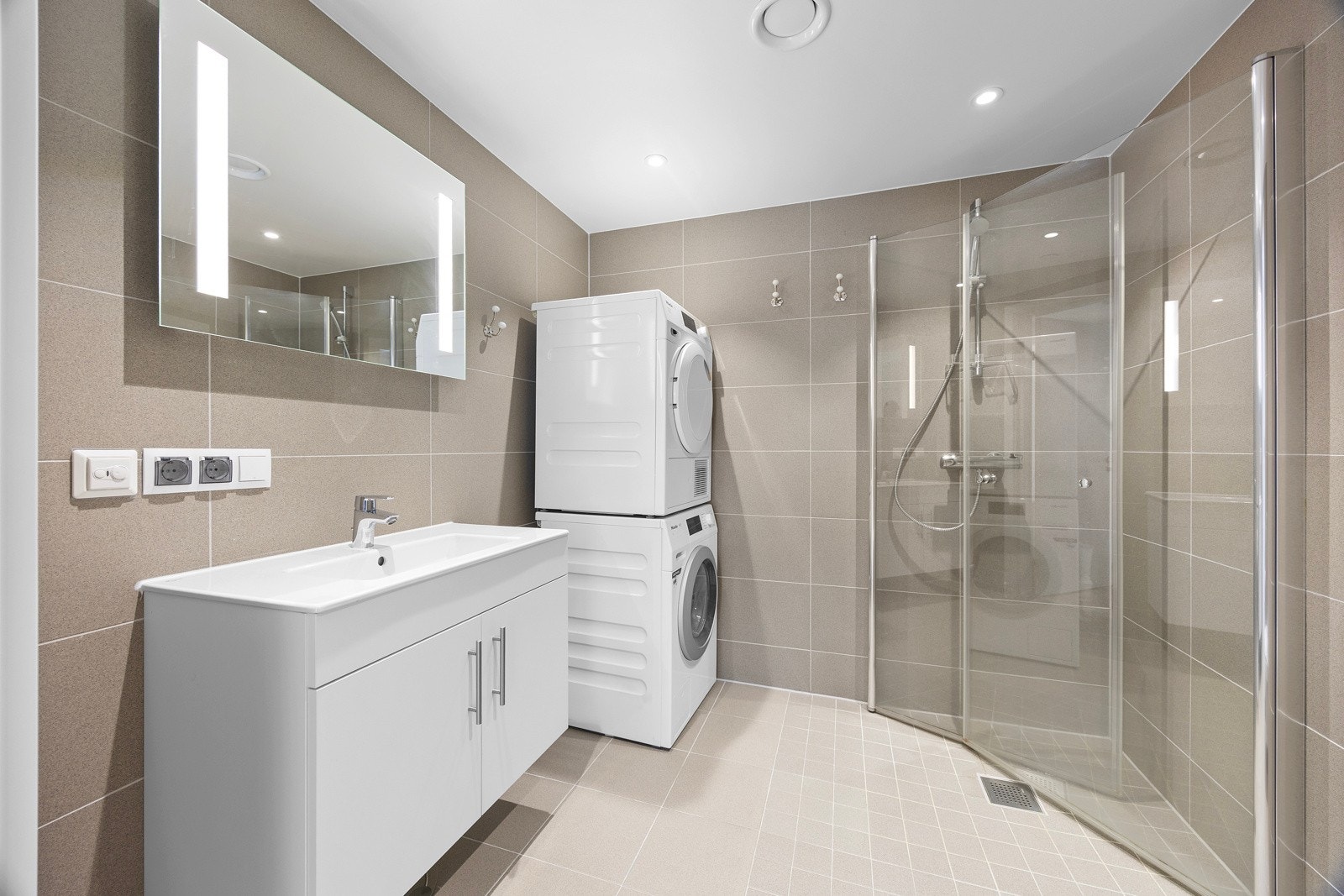 Smakfullt bad med flislagte overflater og varmekabler i gulv. Baderomsinnredningen består av moderne servantmøblement med heldekkende hvit blank vask og speil med integrert LED lys. Galleribilde