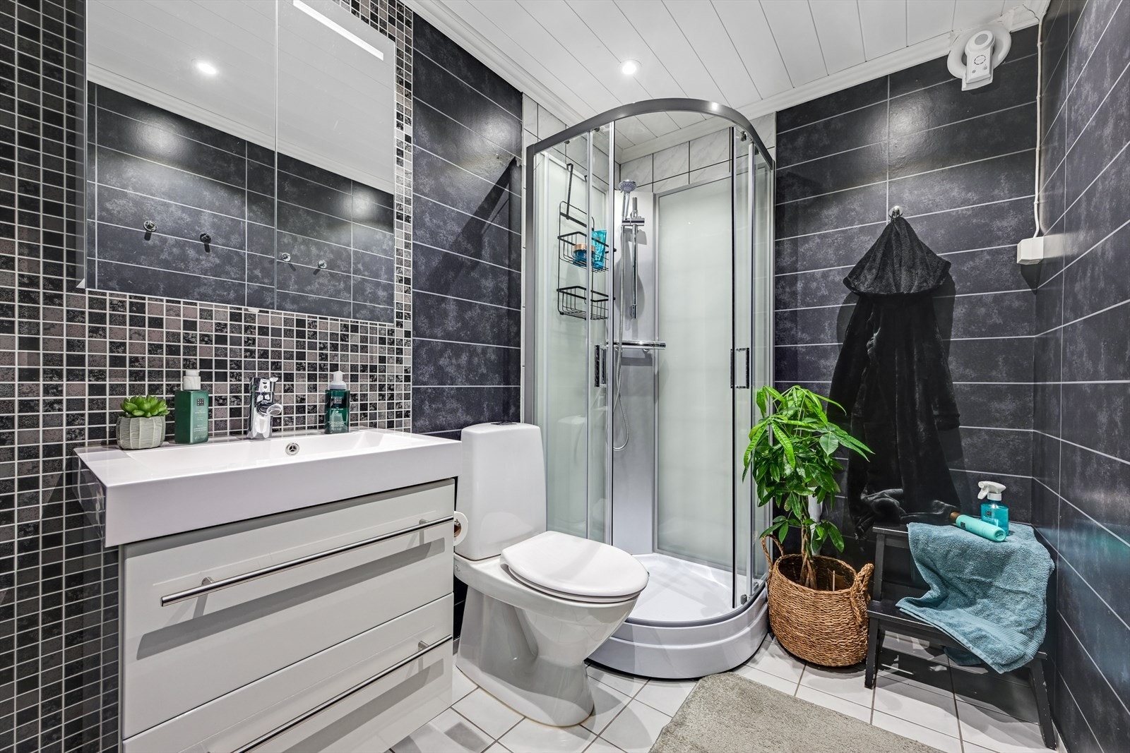 Bad/wc med helstøpt servant i innredning med skuffer, toalett og dusjkabinett. Opplegg for vaskemaskin. Mekanisk vifte på vegg. Galleribilde