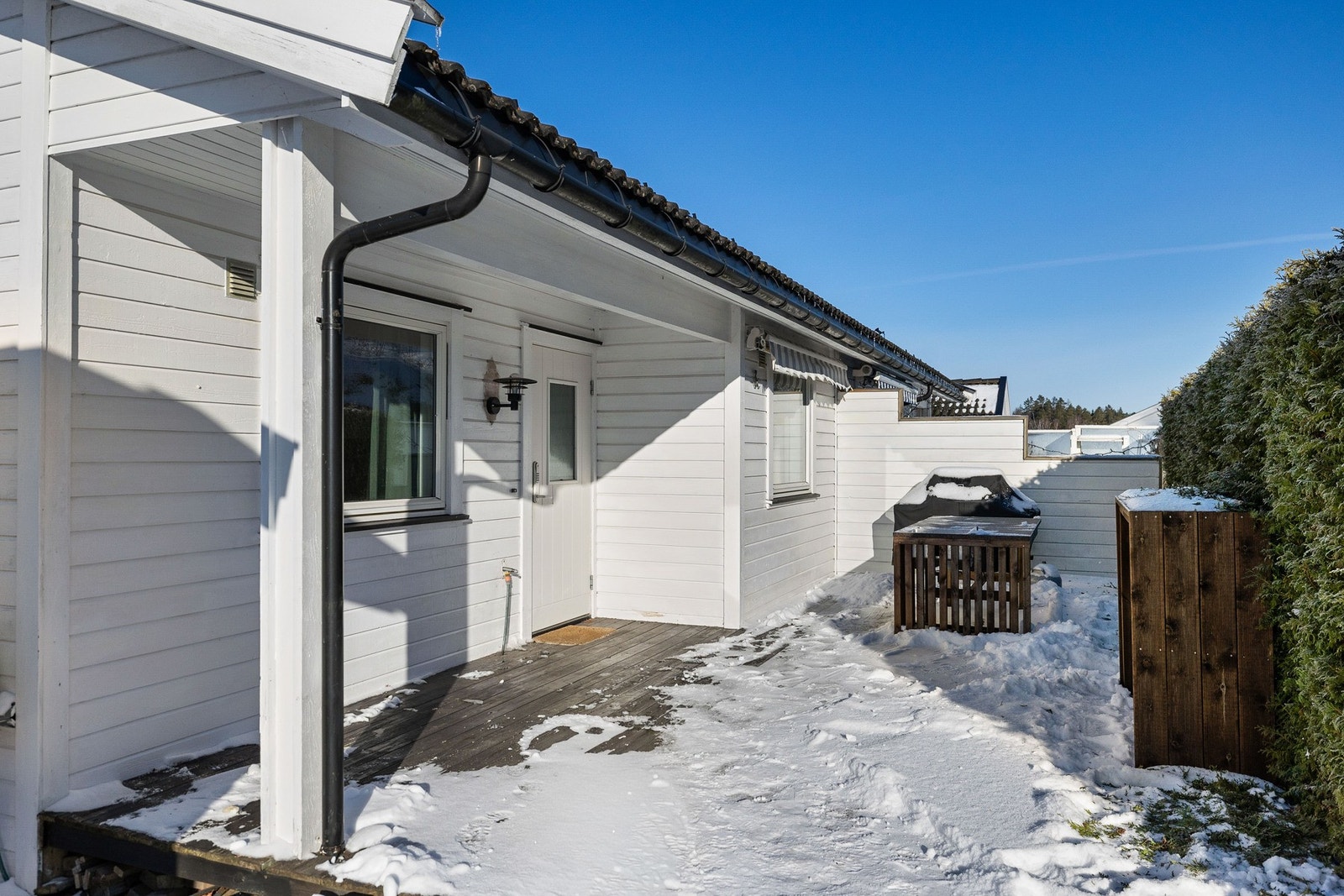 Inngangsparti med platting. Uteområdet har plass til gril og er skjermet mot veien med hekk. Galleribilde