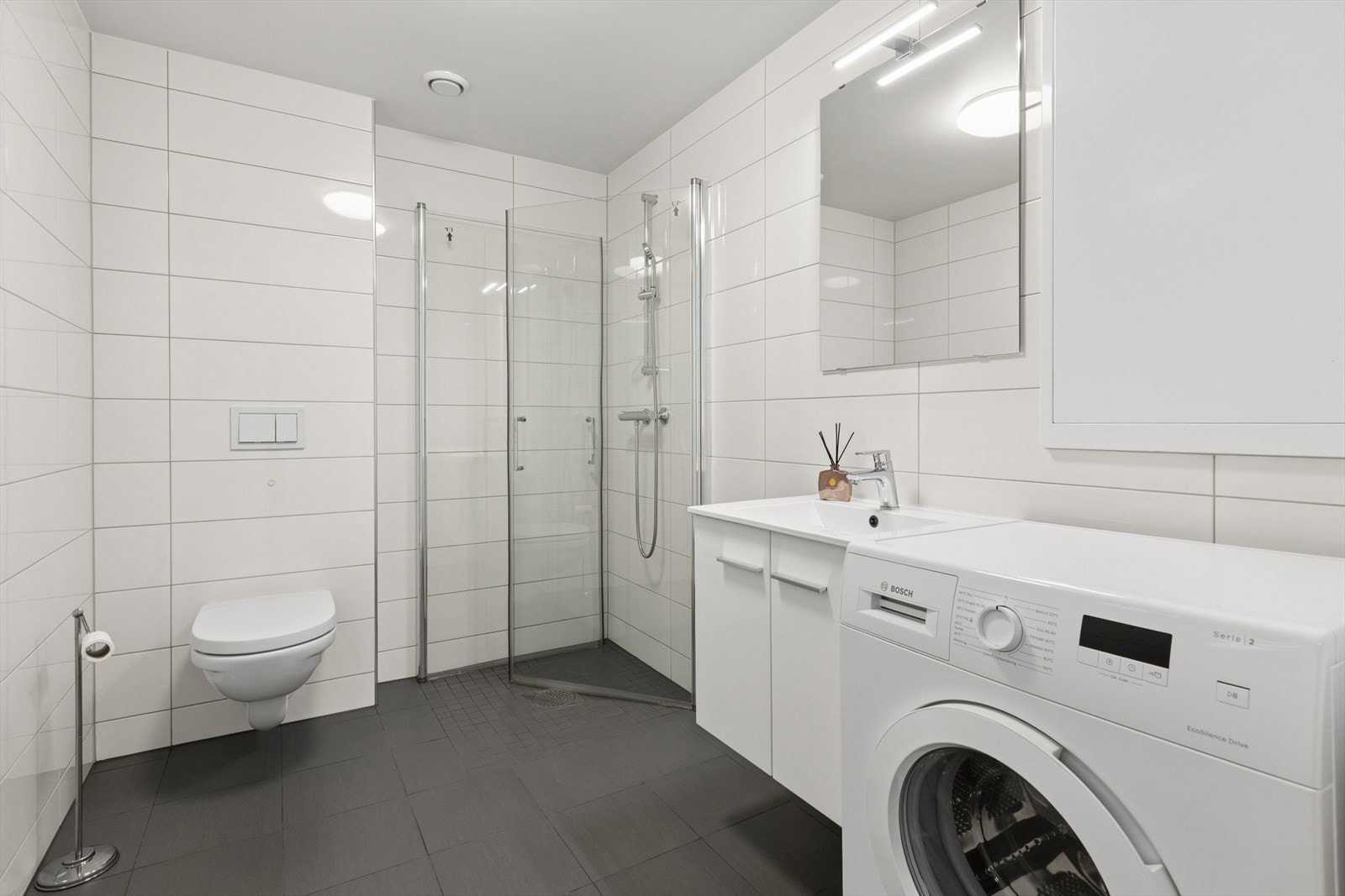 Badet har flislagte overflater med gulvvarme, dusjhjørne med glassvegger og vegghengt toalett. Galleribilde