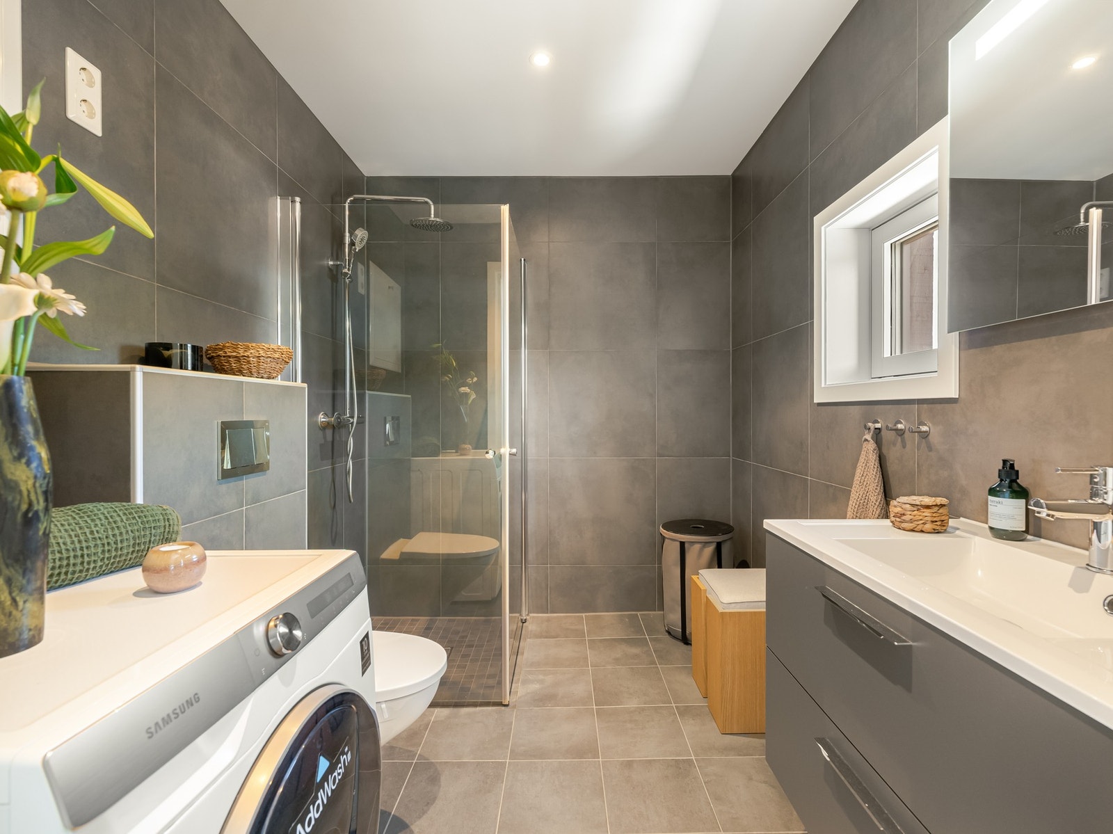 Badet er pent flislagt fra byggeår 2021 og innredet med dusjsone med innfellbare glassdører, vegghengt toalett, servantskap med oppbevaring og speilskap på vegg. Galleribilde