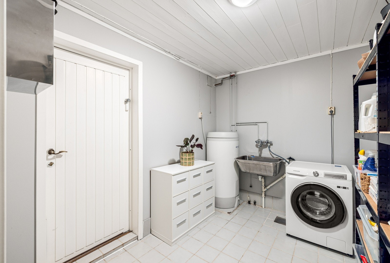 Lyst og praktisk vaskerom med flislagt gulv og gulvvarme. Rommet har god plass til både vaskemaskin og tørketrommel, samt arbeidsbenk og oppbevaringsløsninger. Galleribilde