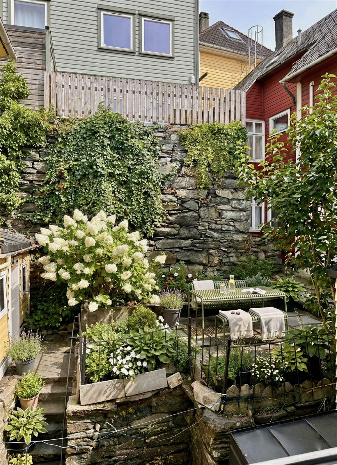 En usjenert og koselig hage med sjel, der en nydelig syrinhortensia setter et frodig preg på uteområdet. Den lune plasseringen mot fjellveggen gjør dette til det perfekte stedet for varme dager og lyse kvelder. Galleribilde