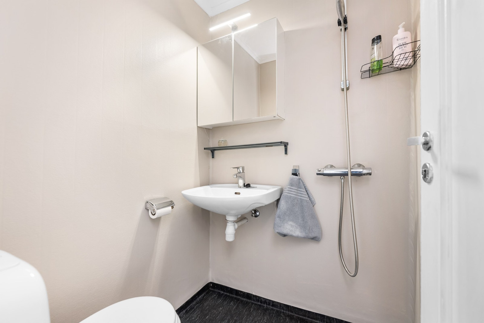 Baderom er fra ukjent eksakt årstall med gulvflate belagt med gulvbelegg. Badet er innredet med vegghengt servant med armatur, speilskap med overlys, dusjhjørne med forheng og gulvstående toalett. Galleribilde