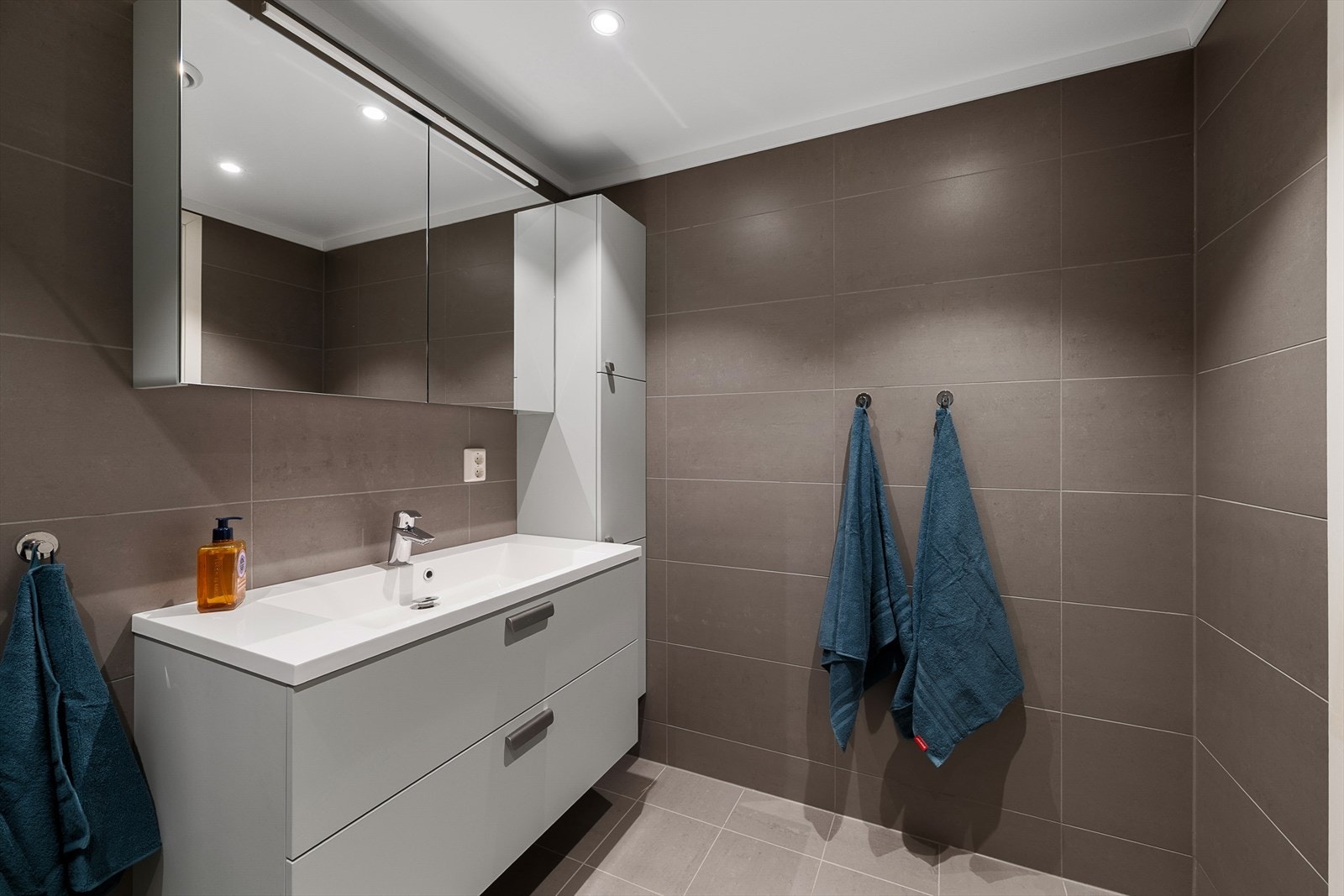 Baderomsinnredningen er stilren med porselensvask og et praktisk høyskap for oppbevaring. Galleribilde