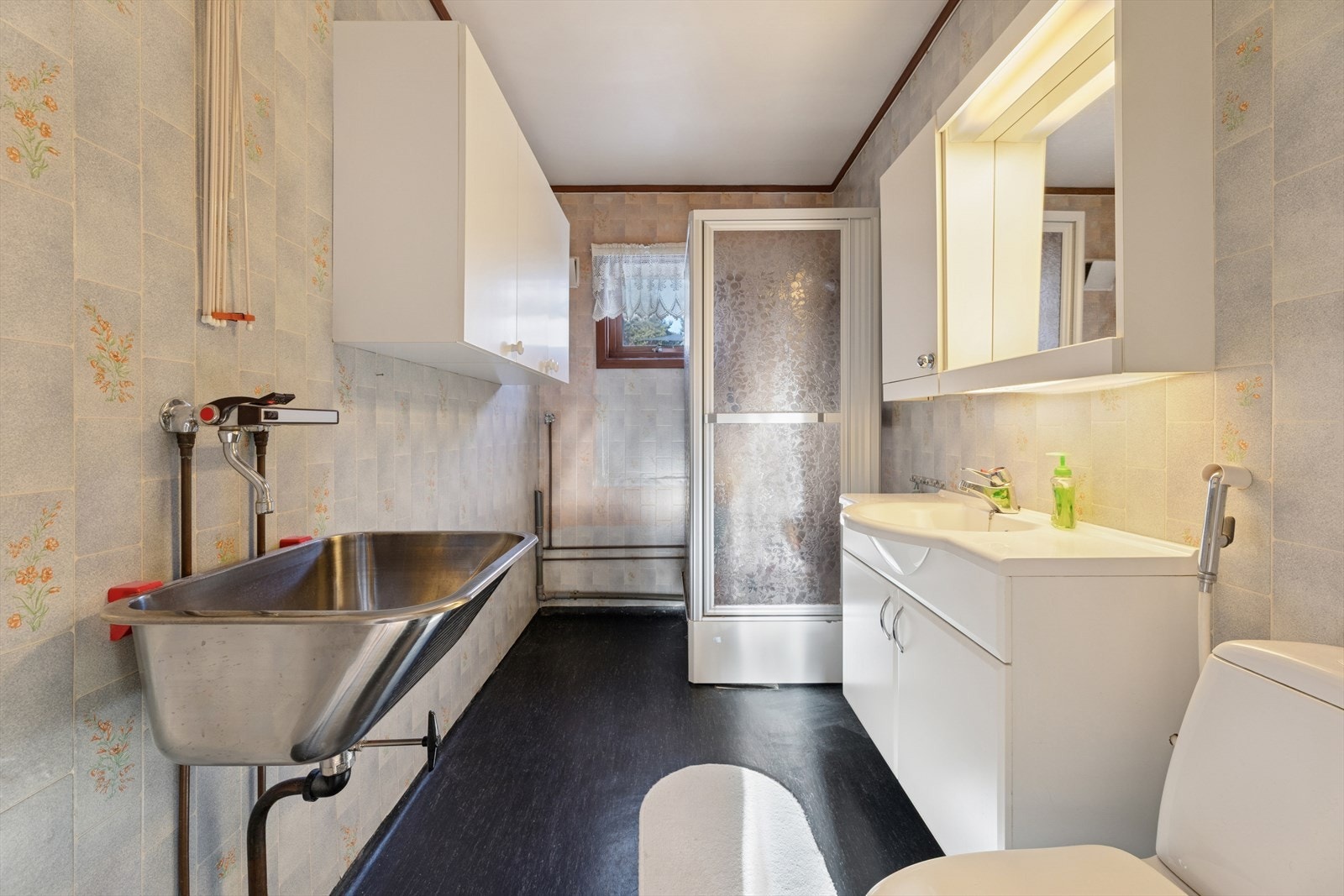 Rommet er innredet med dusjkabinett, servant over innredning med skap, speilskap med belysning, vegghengt skap, toalett, skyllekum og opplegg for vaskemaskin. Galleribilde