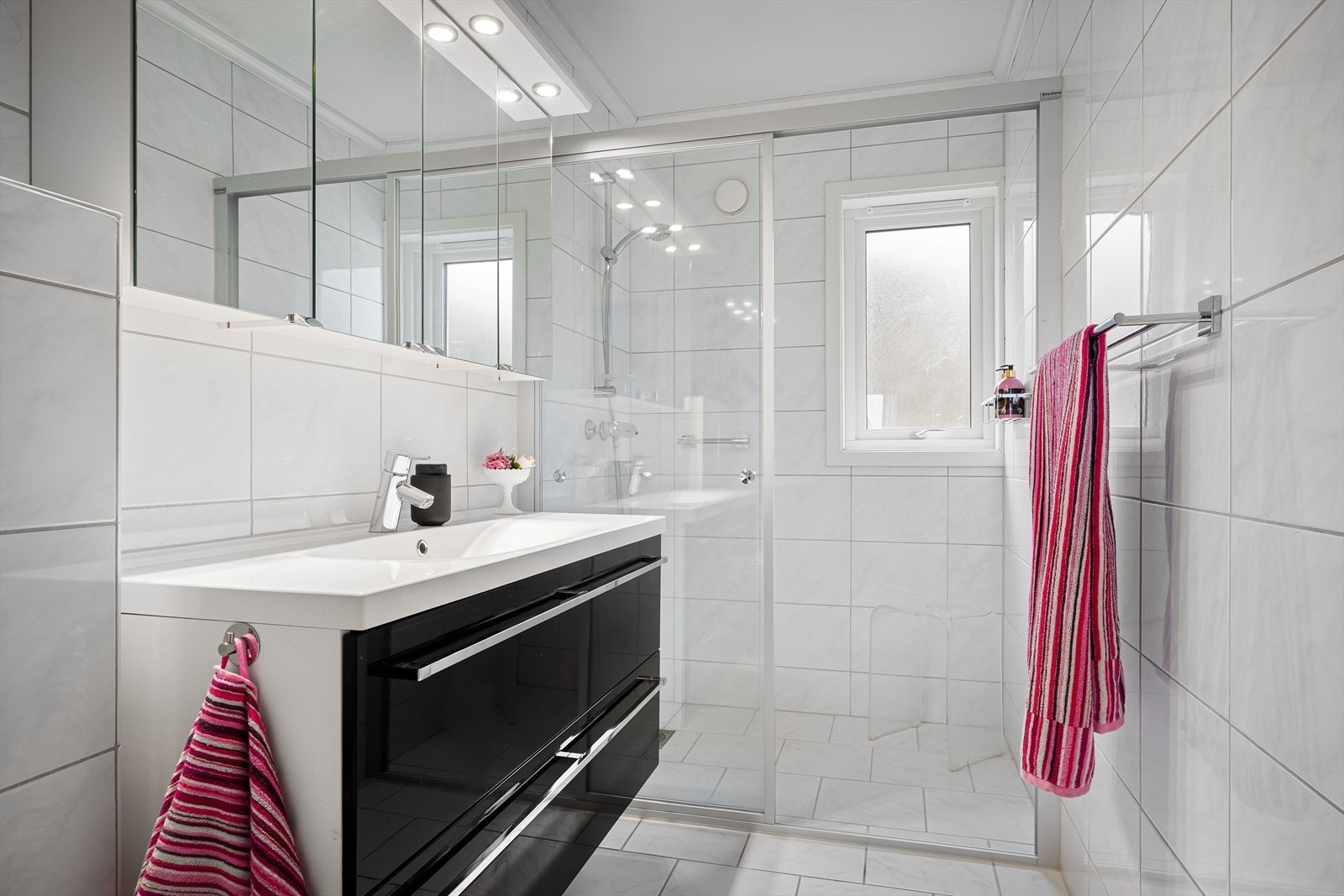 Et tidløst og moderne baderom med romslig dusjhjørne med plass til dusjstol. Speilskap i tillegg til seksjon gir god oppbevaring. Galleribilde