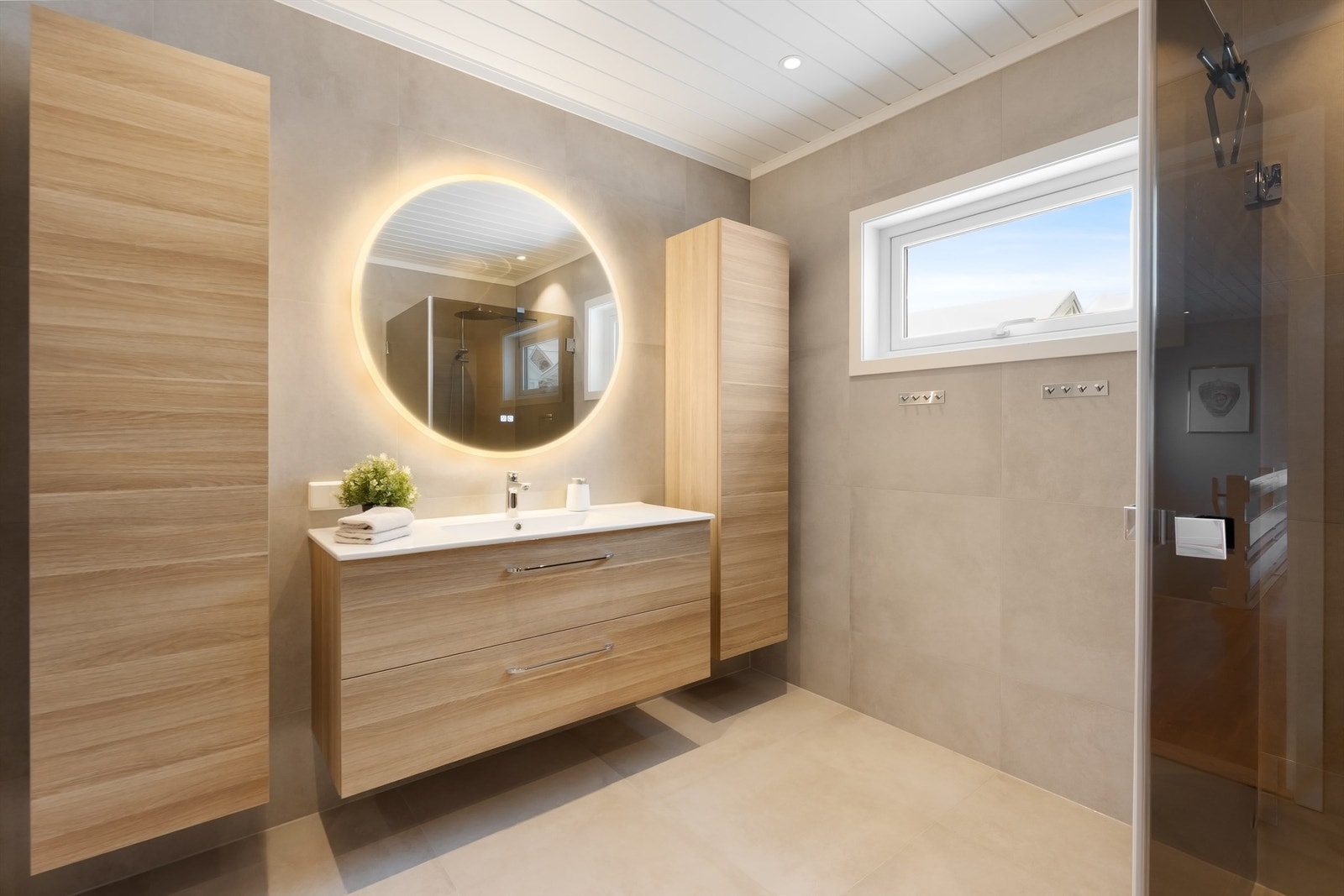 Innredningen inkluderer en bred, vegghengt servant med skuffer og et speil med integrert belysning. Galleribilde