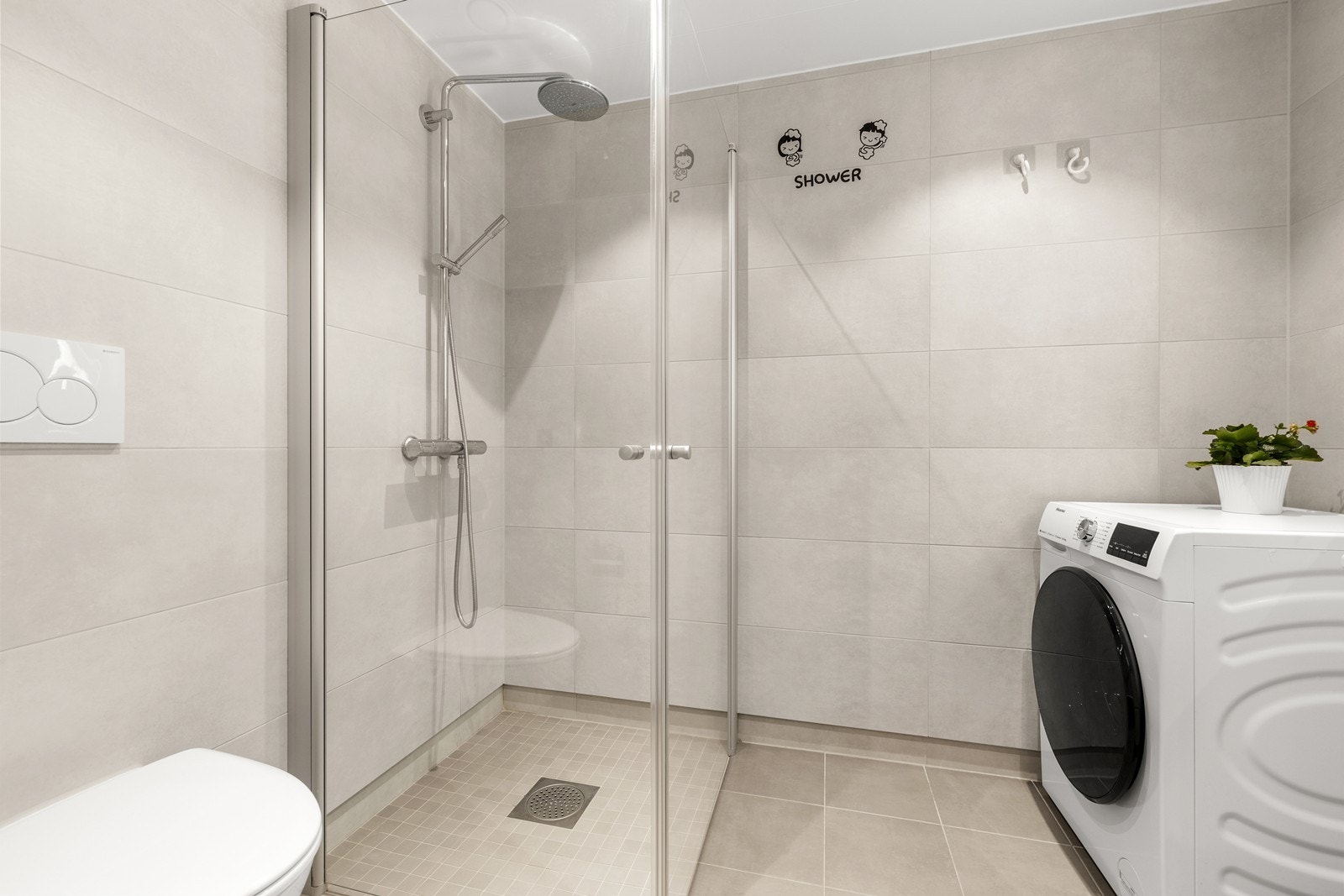 Dusj med innfellbare glassvegger, vegghengt toalett og opplegg for vaskemaskin. Galleribilde