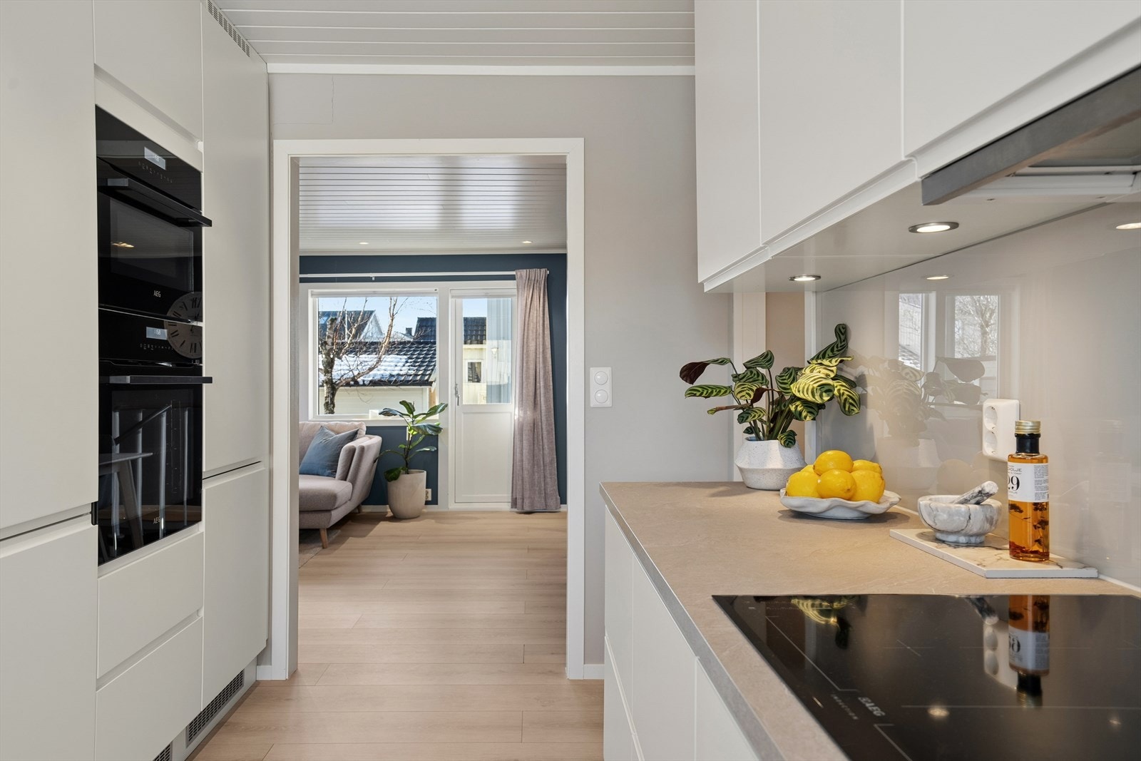 Kjøkkenet ble modernisert i 2019 og har en moderne innredning - Det er hvite glatte fronter, benkeplate i laminat og glassplate på vegg over benk Galleribilde