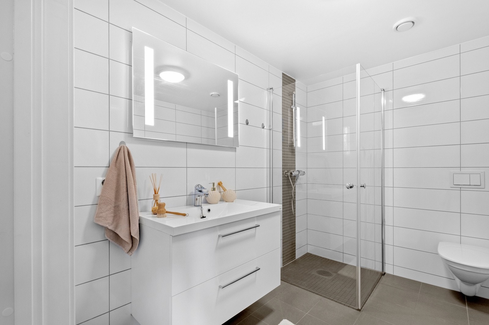 Flott, flislagt bad utstyr med varme i gulv, servant med skuffer, dusjhjørne, opplegg for vaskemaskin og toalett. Galleribilde