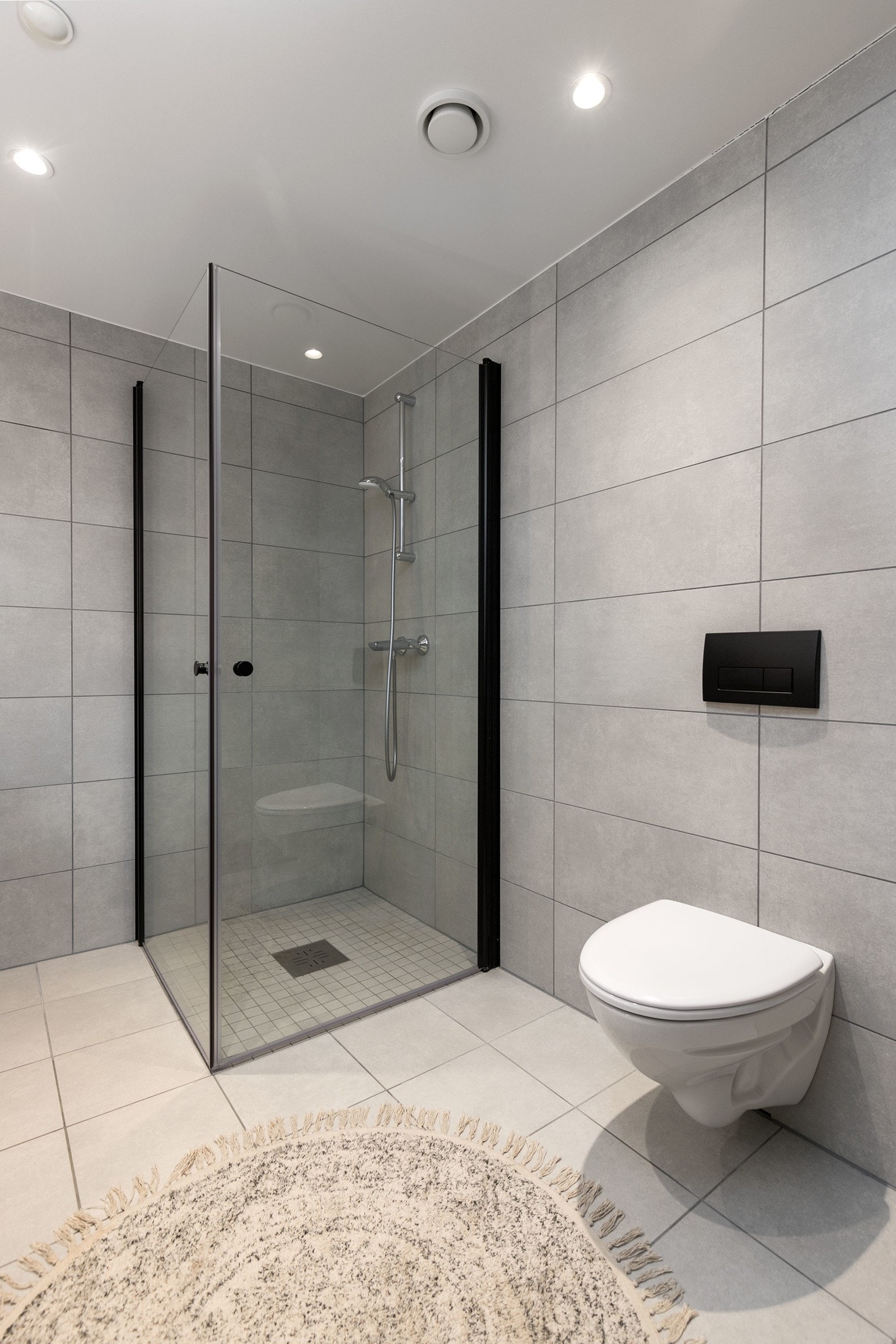 Delikat flislagt bad med vegghengt toalett, dusjsone med innfellbare dører samt servant med skapinnredning. Galleribilde