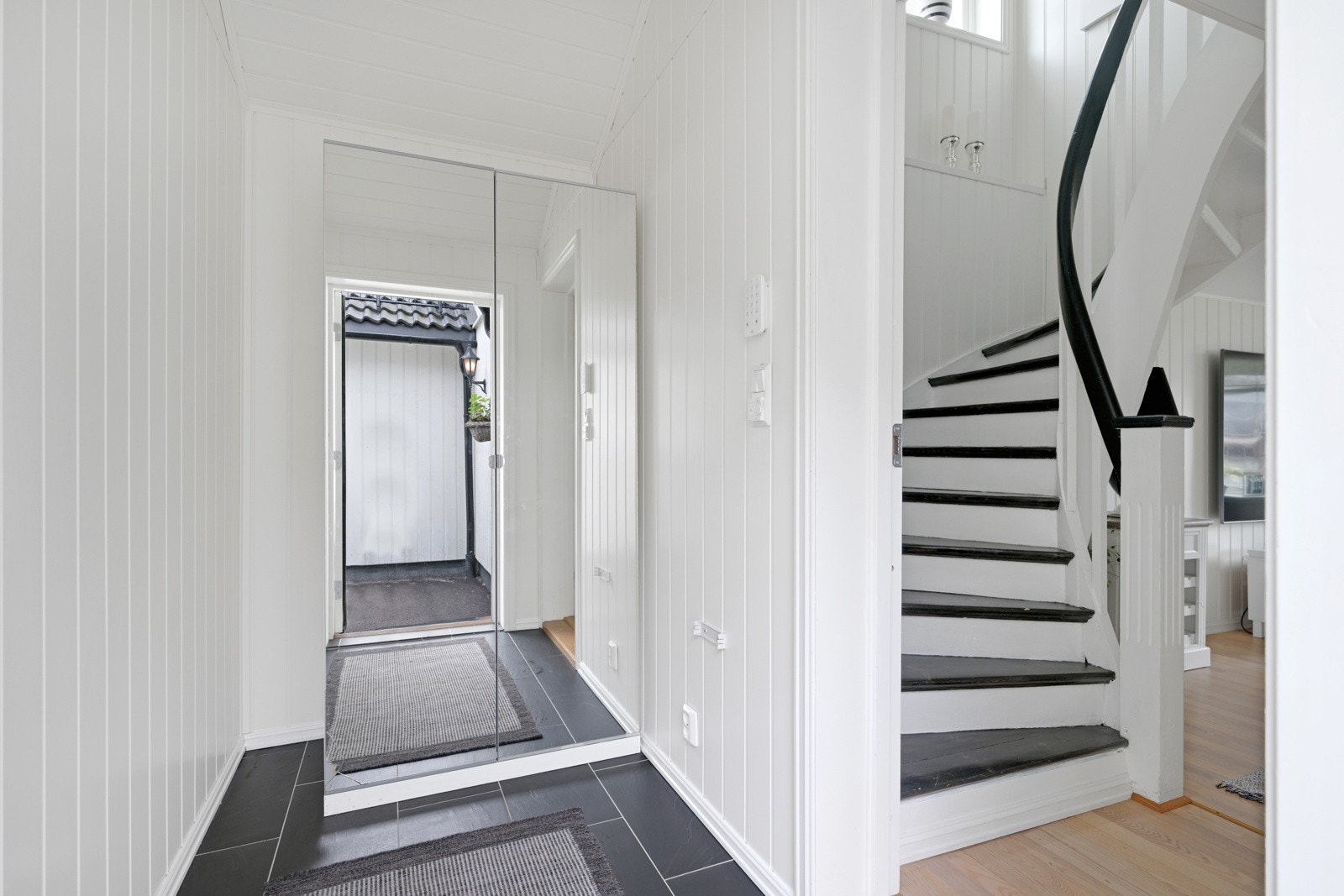 Velkommen inn i en lys entrè med flislagt gulv og panel på vegg Galleribilde