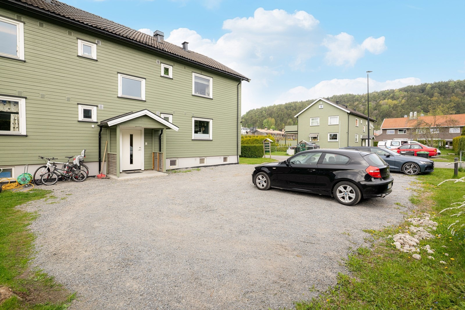 Felles, asfaltert biloppstillingsplass i front av firemannsboligen, rett ved inngangsdøren. Galleribilde