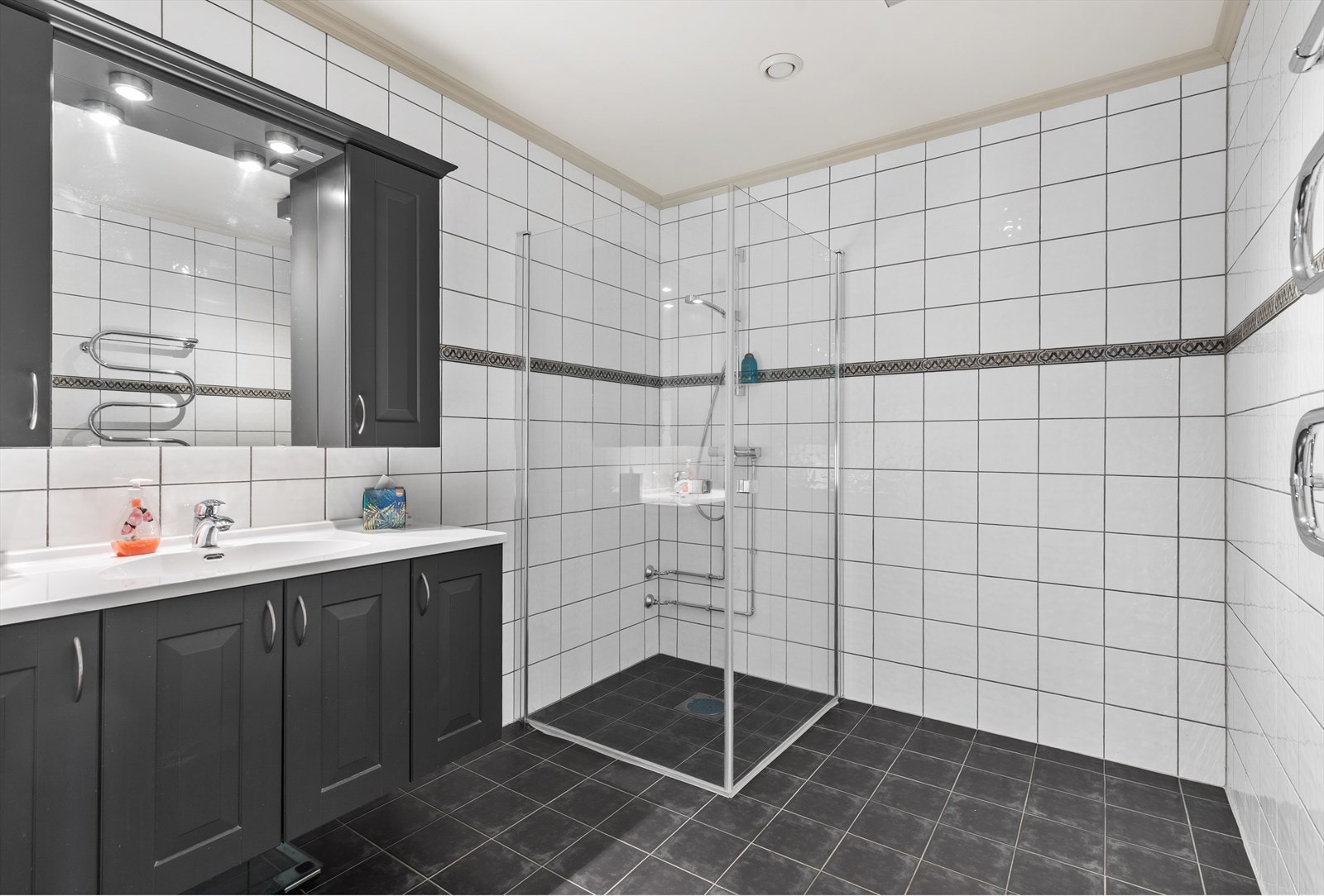 Flislagt baderom innredet med nedfelt servant med underskap, overskap med speil og dusjhjørne. Galleribilde