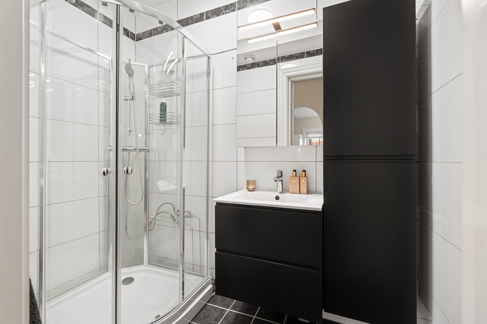 Pent, flislagt bad fra ca. 2010 med dusjkabinett og moderne baderomsinnredning fra 2023, samt et speilskap for ekstra oppbevaring. Galleribilde