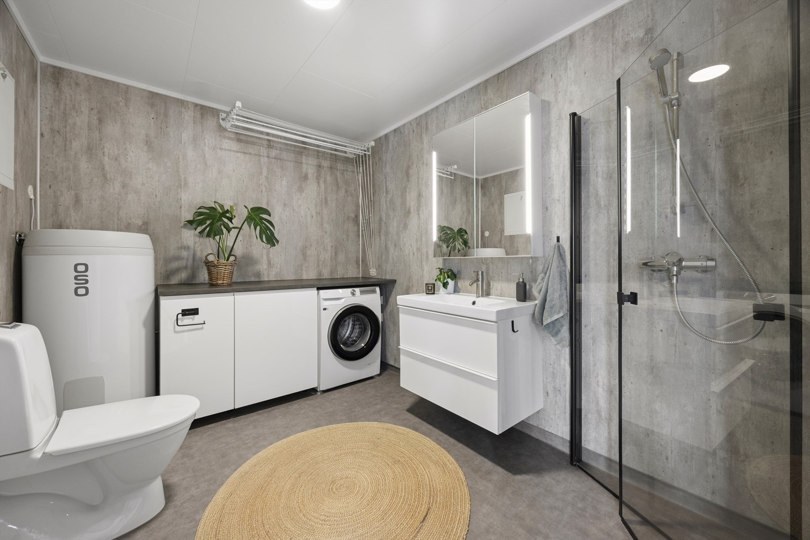 Badet består av speil med belysning, servant med seksjon, toalett, dusjhjørne, benkeplate med skap og opplegg for vaskemaskin. Galleribilde