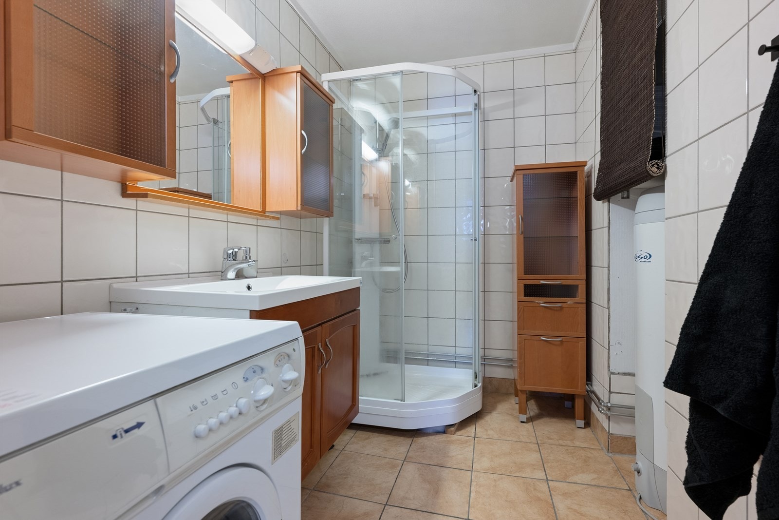 Lyst flislagt bad med behagelige varmekabler i gulv. Badet er utstyrt med dusjkabinett og opplegg for vaskemaskin. Galleribilde