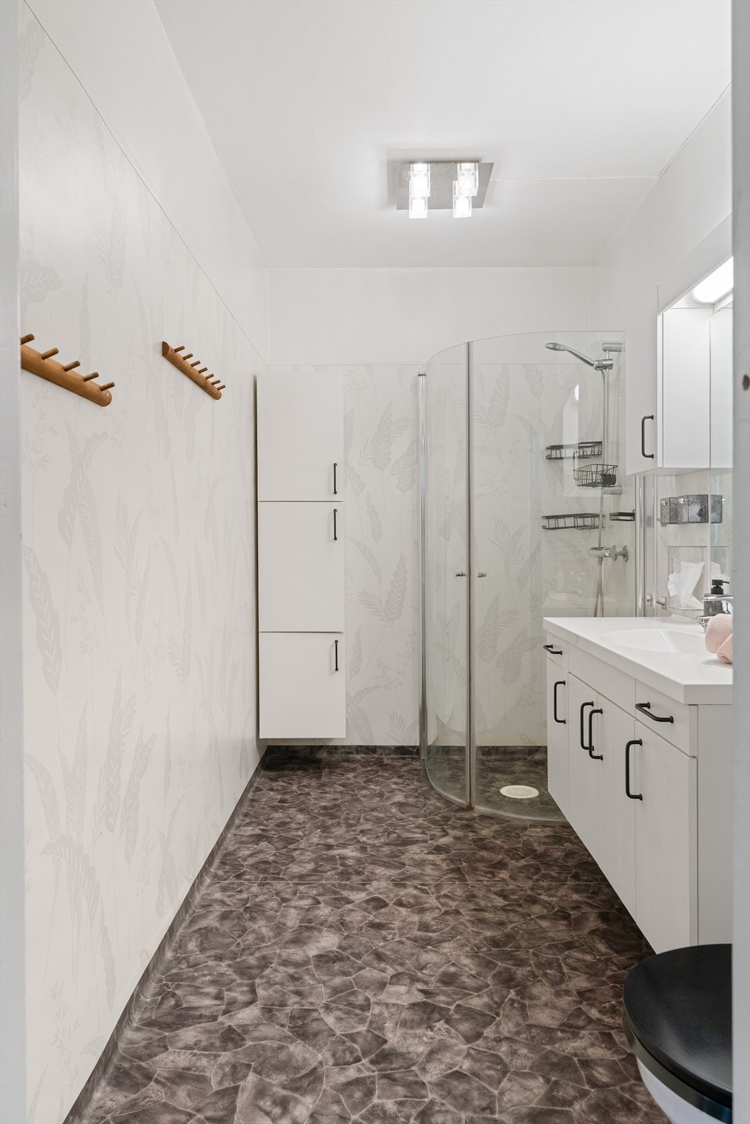 Badet har gulv og vegger belagt med belegg - Dusjhjørne med dører av glass og vegghengt armatur med garnityr - Vegghengt servantinnreding med ett-greps armatur - Vegghengt toalett Galleribilde