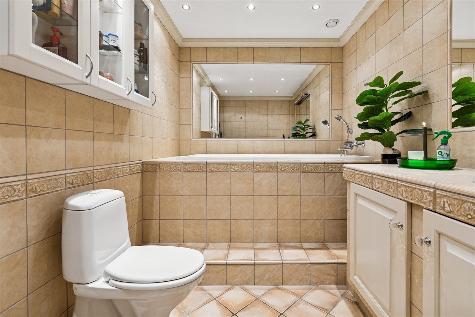 Badet har innfliset badekar, gulvstående toalett og innholdsrik innredning med servant. Galleribilde