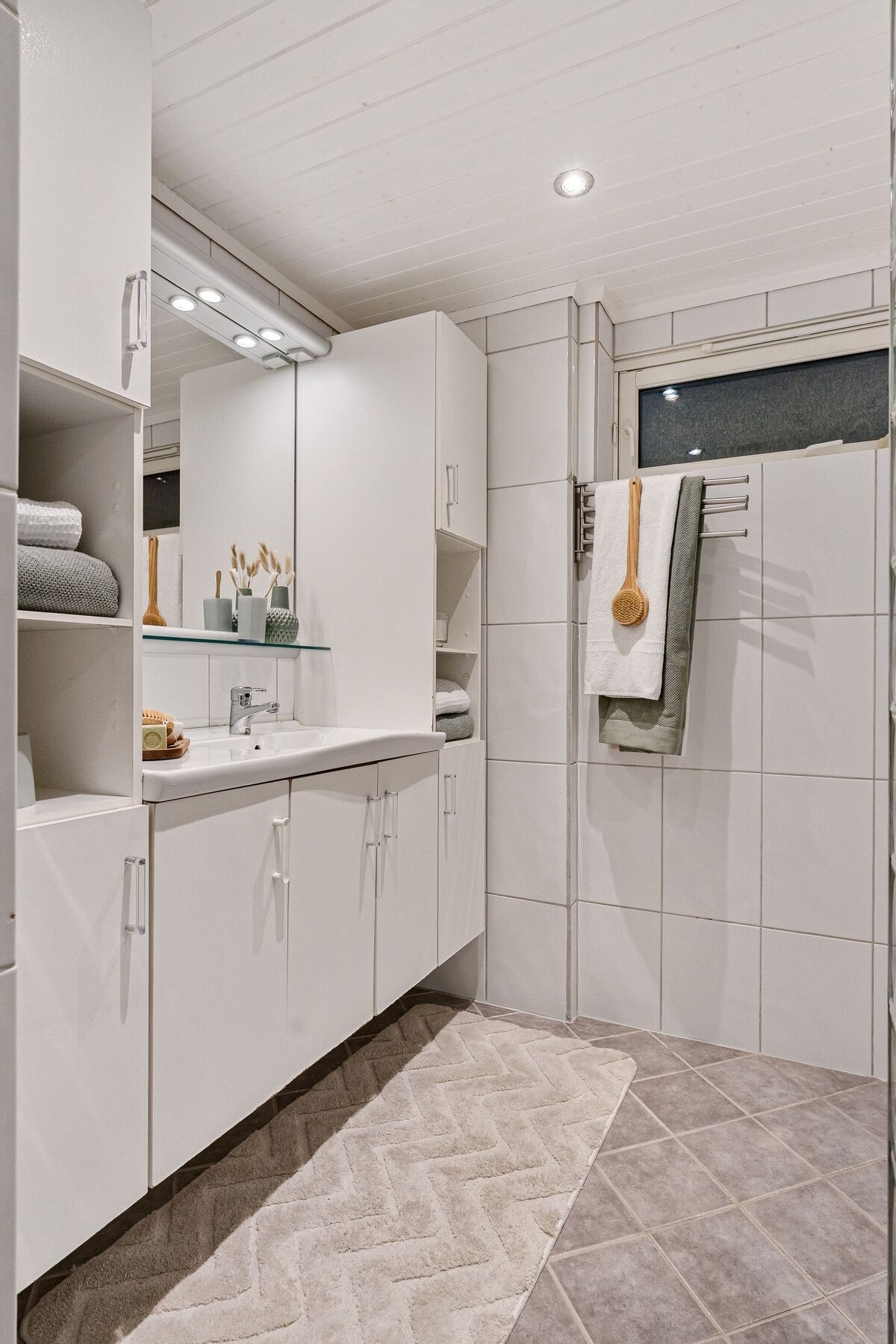 Pent og tidløst flislagt bad utstyrt med dusjhjørne, varme i gulv og servant med over- og underskap med rikelig av oppbevaringsplass. Galleribilde