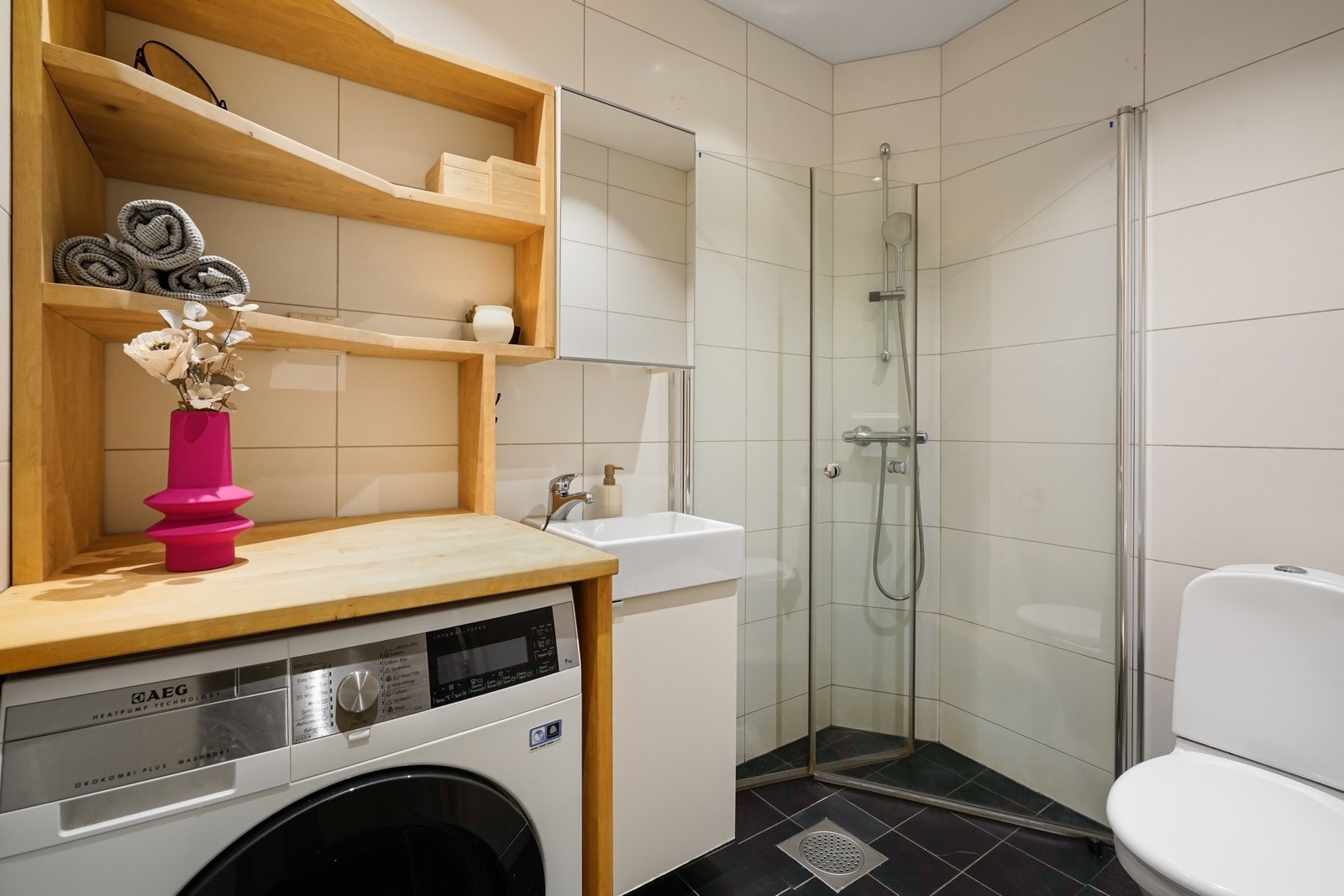 Flislagt bad med praktisk vaskenisje med opplegg for vaskemaskin, benkeplate og hyller, godt egnet for oppbevaring av håndklær, vaskemidler m.m. Galleribilde