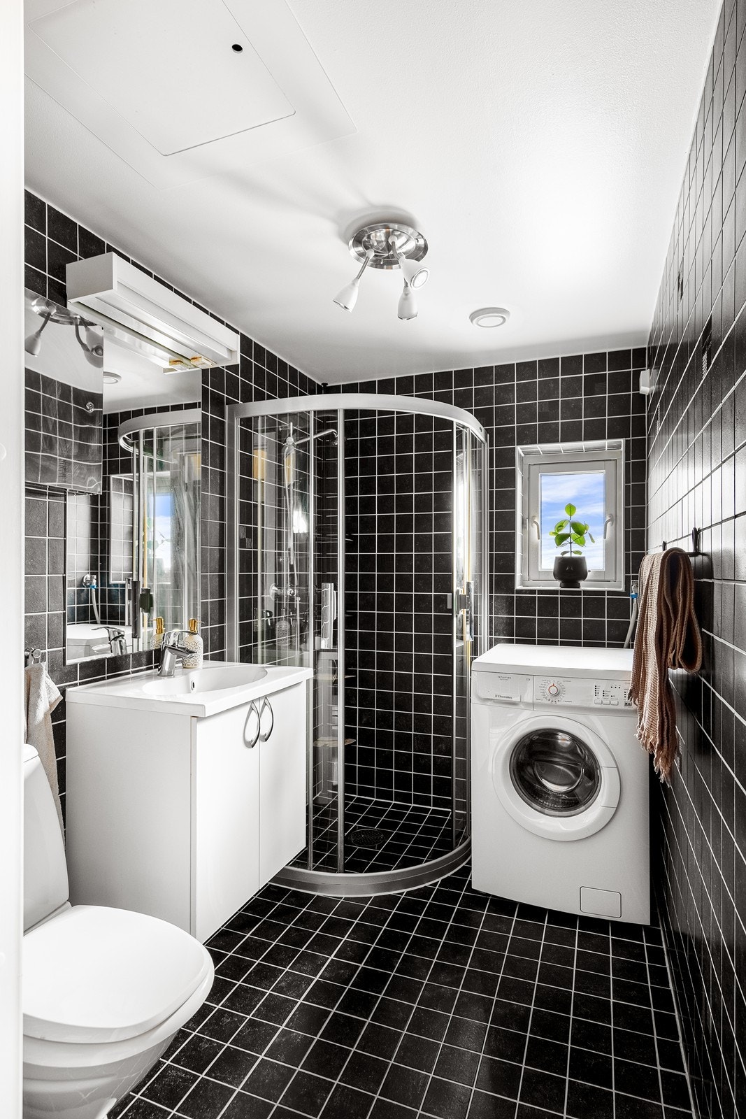 Flislagt bad med gulvvarme. Baderomsinnredning består av servant i seksjon med speil og overlys, oppbevaring under vask, toalett og dusjhjørne. Her er det opplegg til vaskemaskin. Galleribilde