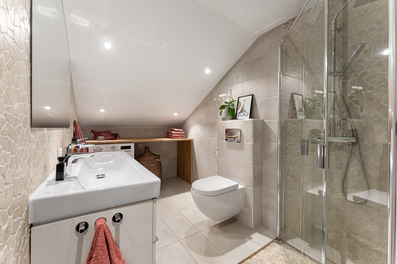 Bad fra 2016 med dusj med innfellbare dører i herdet glass, servant i helstøpt plate, veggfestet toalett og opplegg for vaskemaskin. Galleribilde