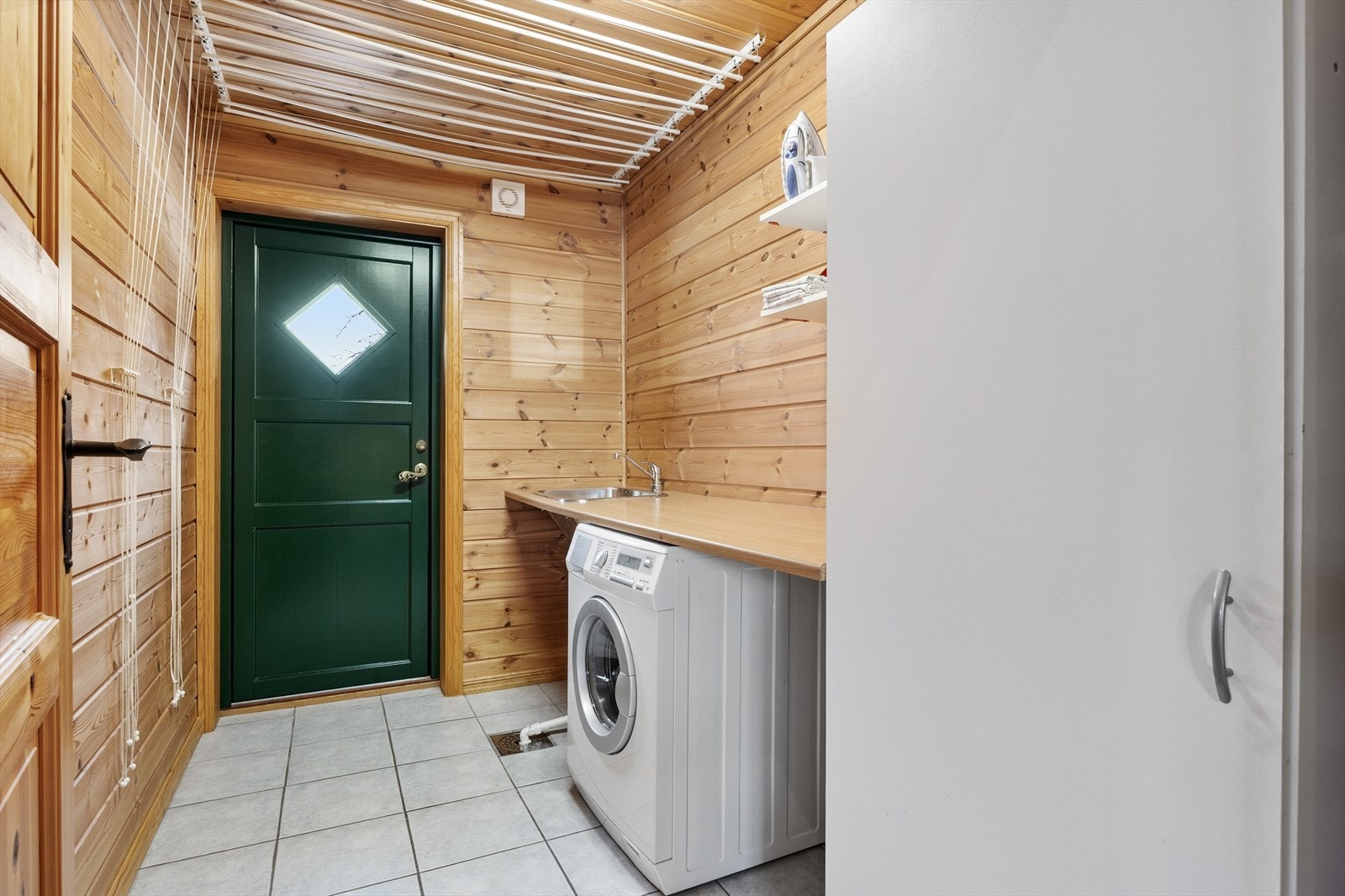 Praktisk vaskerom med flislagt gulv, gulvvarme, utslagsvask og opplegg for vaskemaskin. Galleribilde