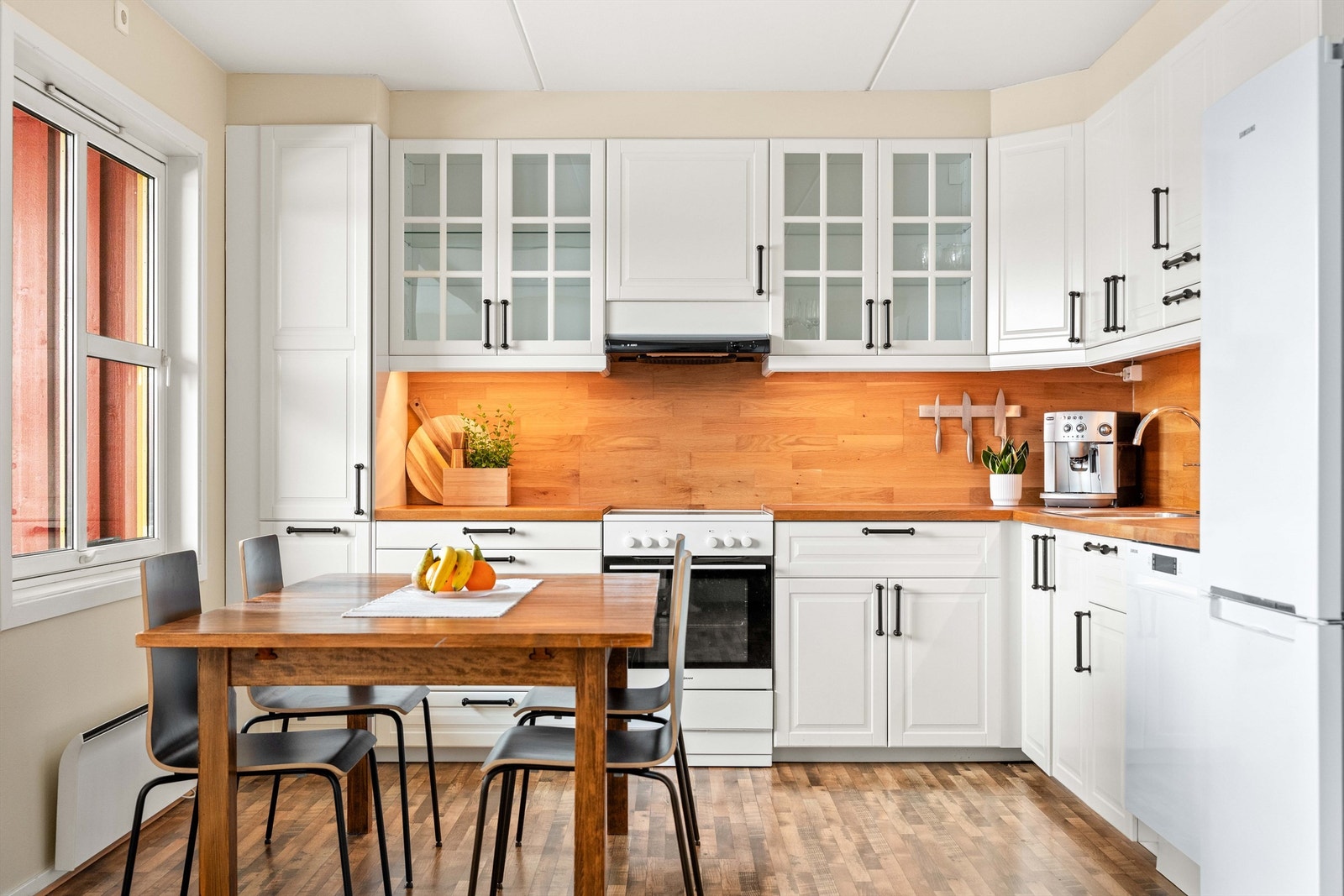 Kjøkkenet har en praktisk hjørneløsning med hvite, profilerte fronter og benkeplate i heltre. Galleribilde