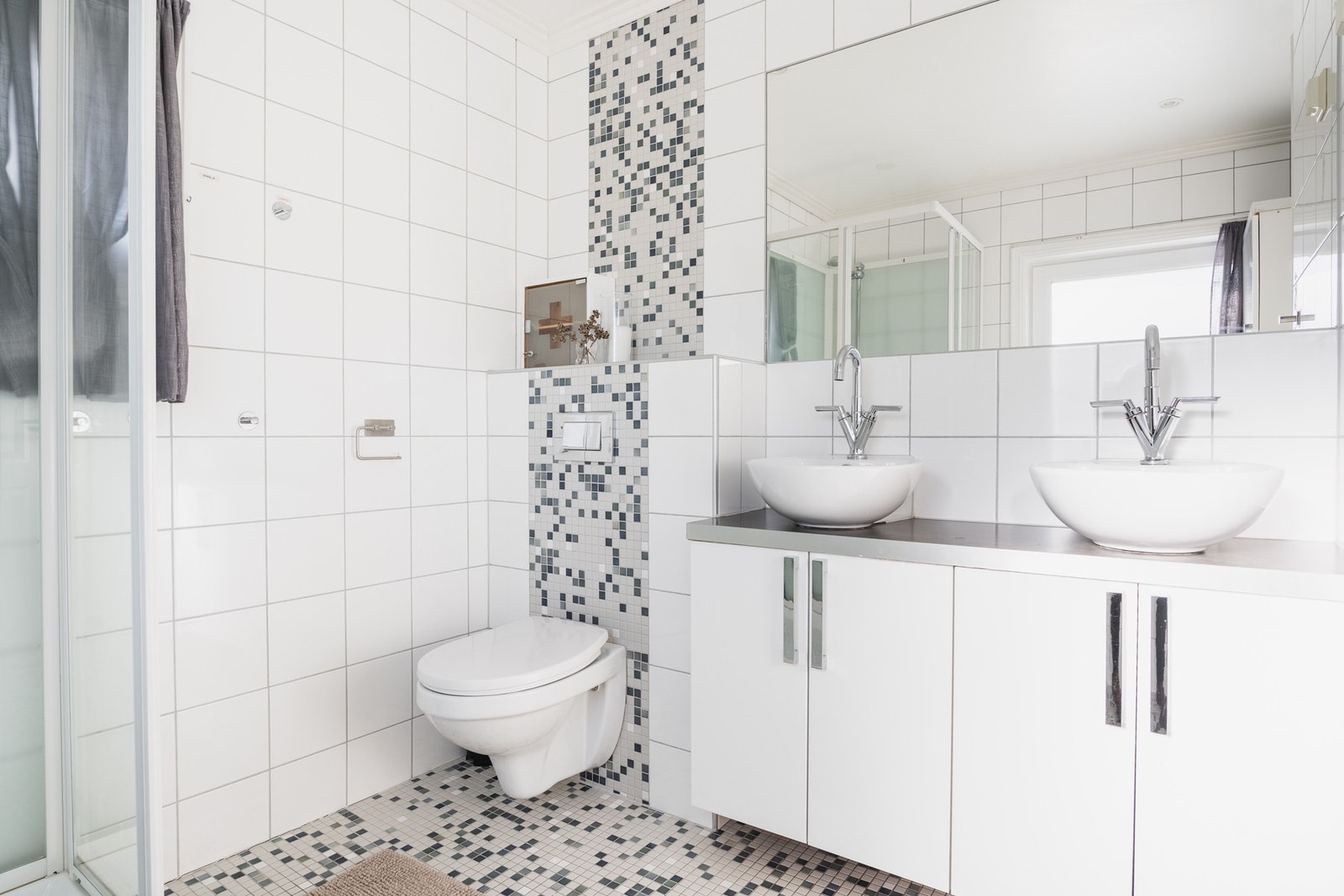 Hovedbad med flislagt gulv og vegger, baderomsinnredning, dusjkabinett, vegghengt toalett og dobbel servant med underskap og speil. Galleribilde