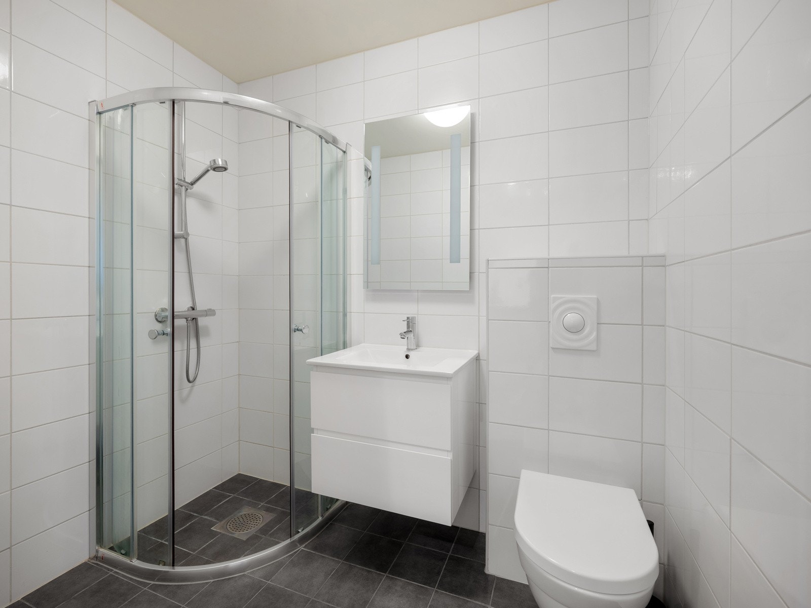 Badet er flislagt og innredet med servant, dusjkabinett og vegghengt toalett. Galleribilde